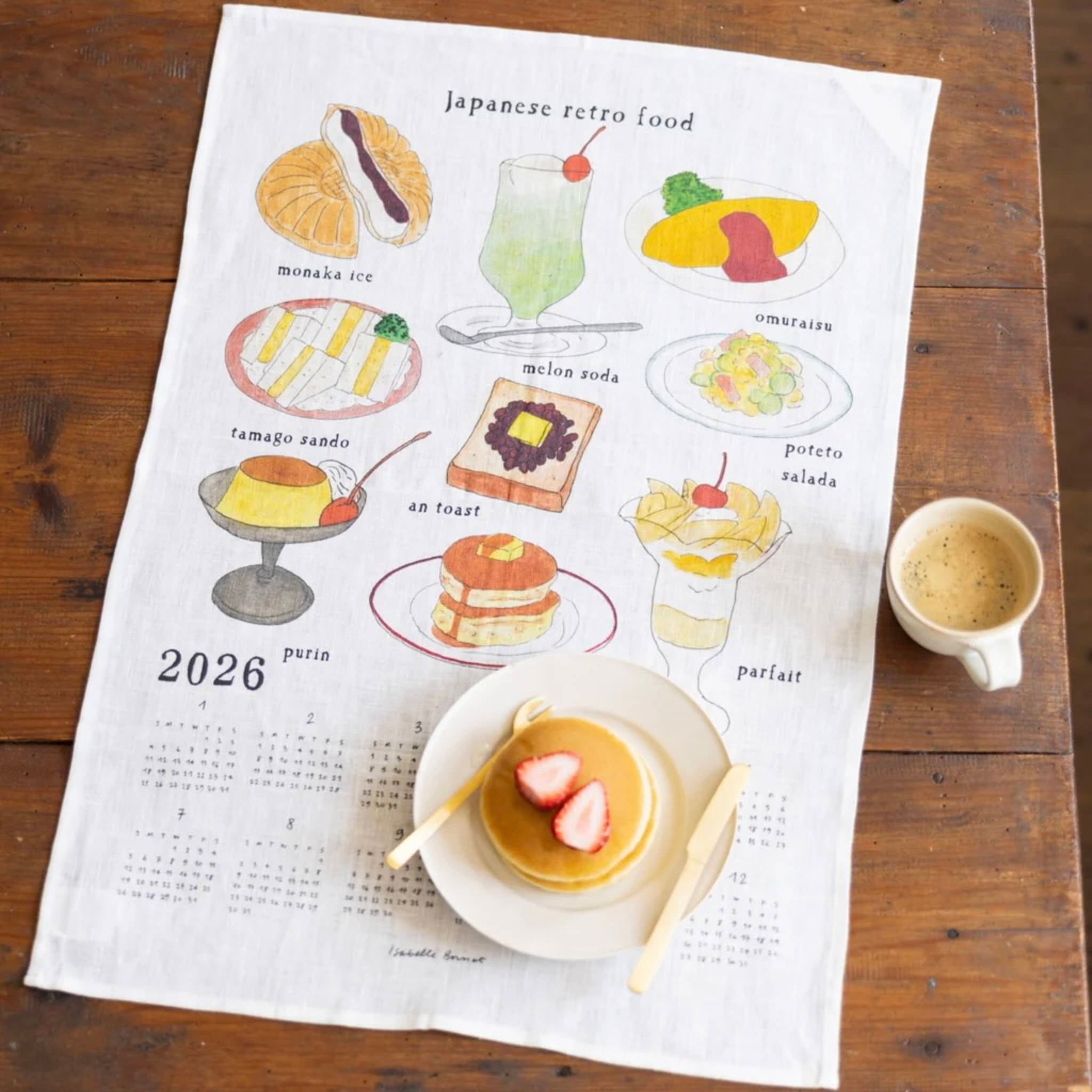 Tea towel with illustrations of Japanese retro food on a wooden table with a cup of coffee.