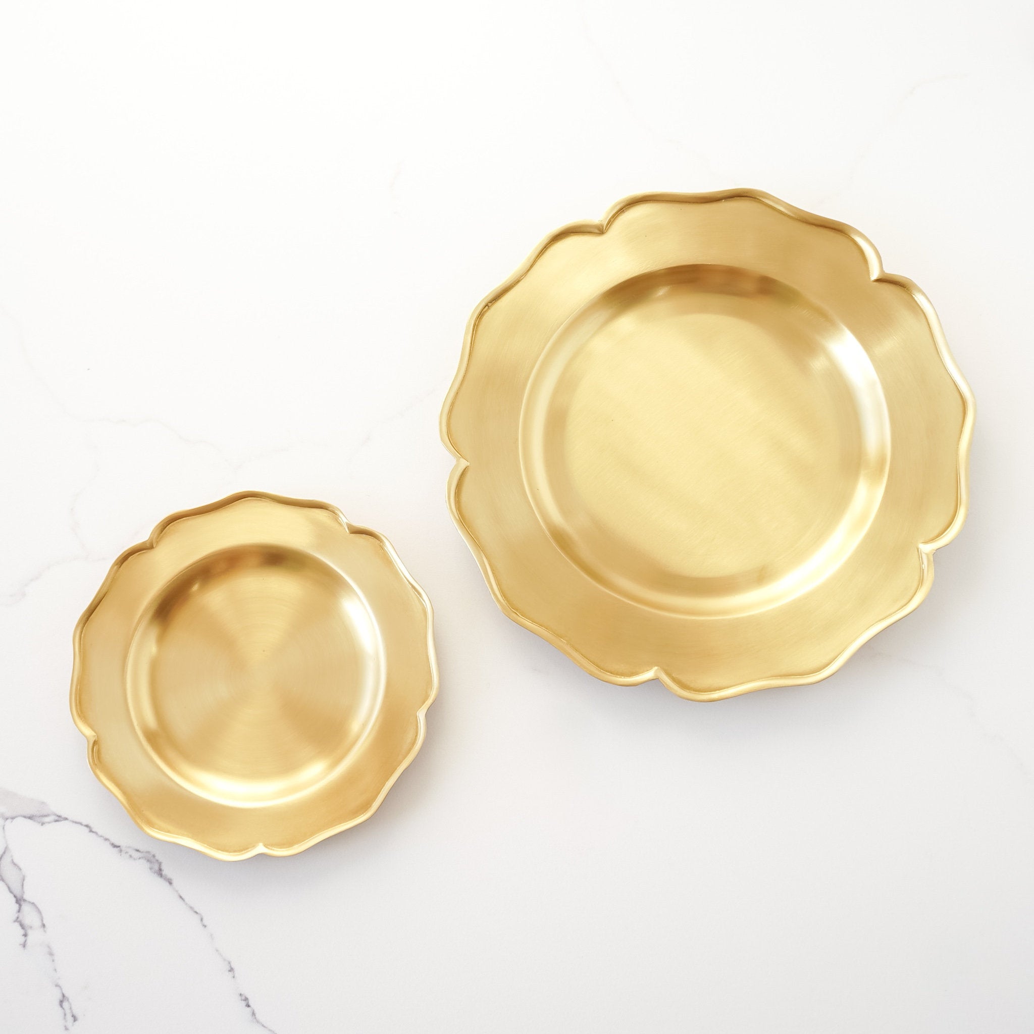 Two antiqued brass trays with ruffled edges, one small and one medium-sized, on a white background.