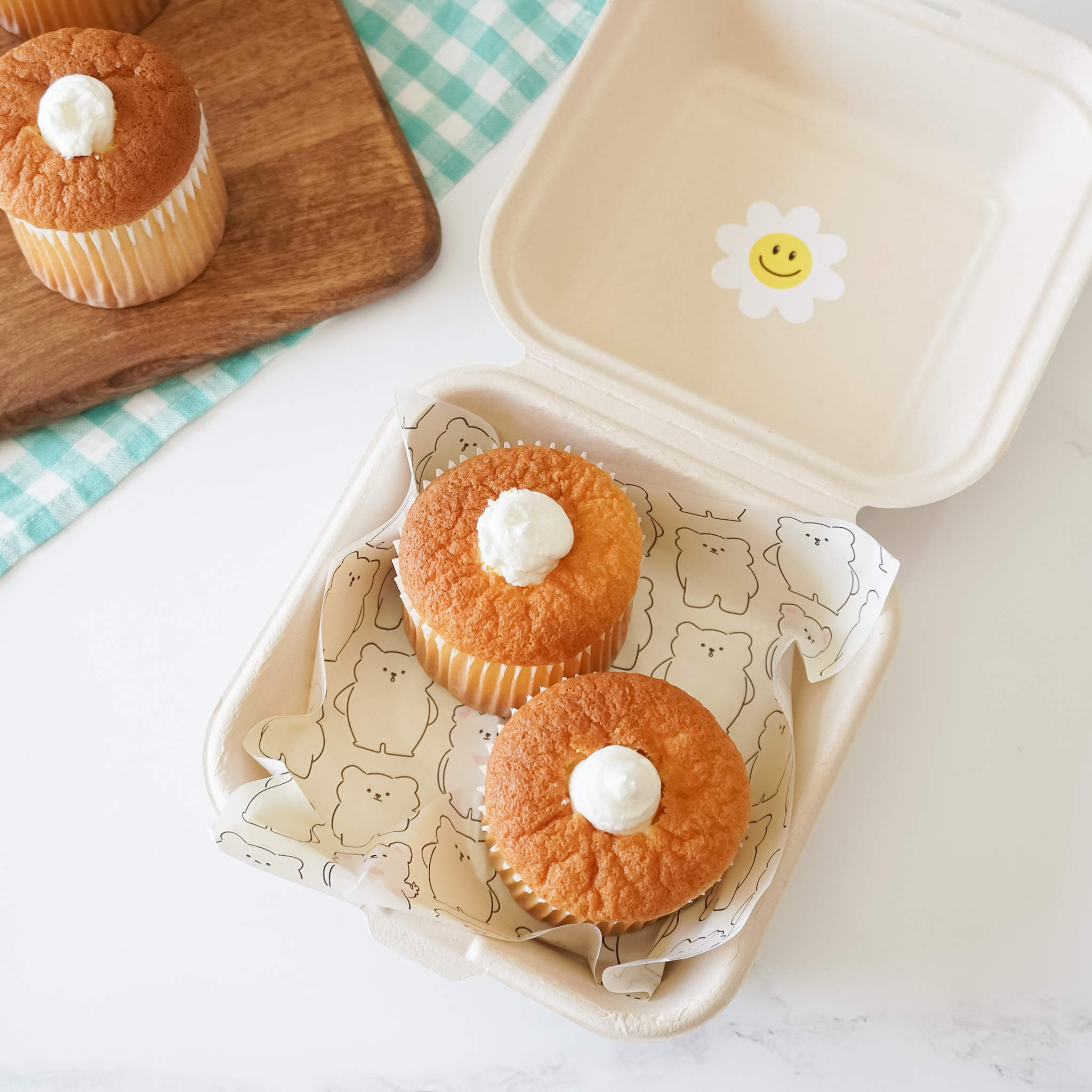 A packaged food item, resembling a cupcake, is presented inside an ivory deli paper with a bear printed design. The paper is partially opened to reveal the food.