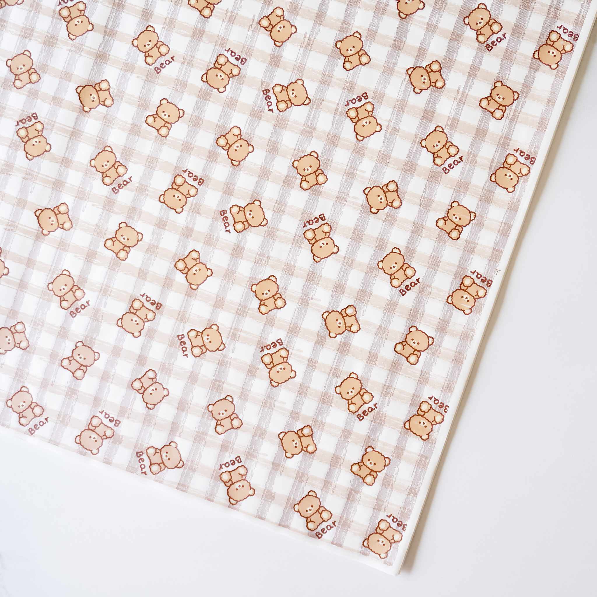 A sheet of deli paper with a brown checkered pattern and cute bear illustrations on it, pre-cut for wrapping.