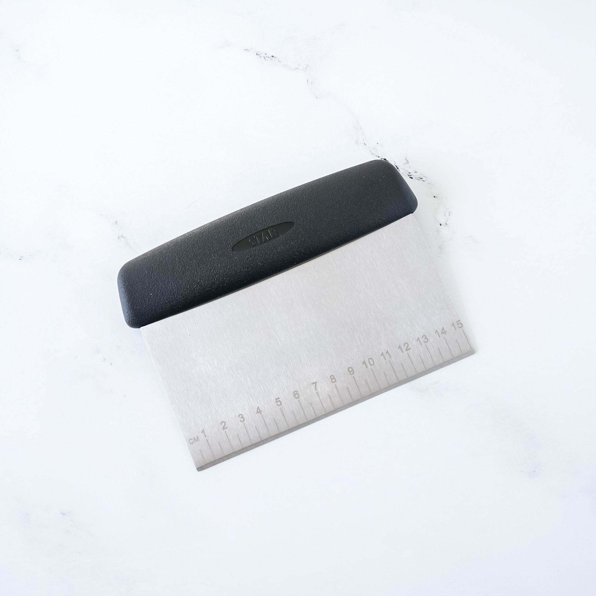 A stainless steel bench scraper with a black non-slip handle and 0.5 cm measurement markings on the blade.