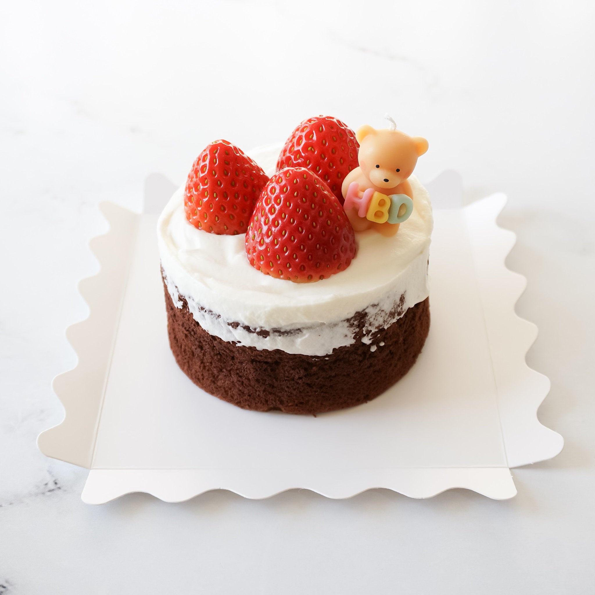 A small birthday cake with white frosting and strawberries on top, garnished with a cute bear candle.