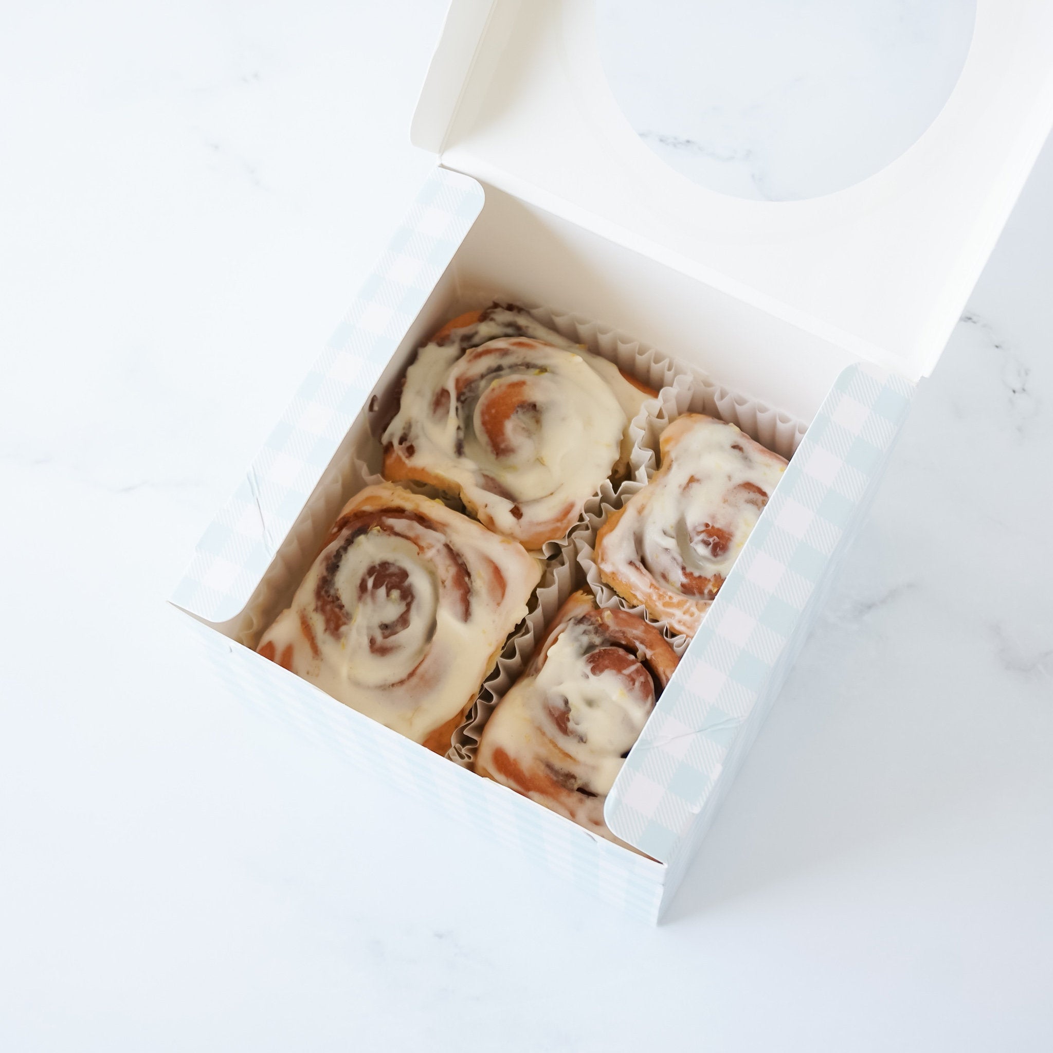 Four white frosted cinnamon rolls in a white and blue checkered box.