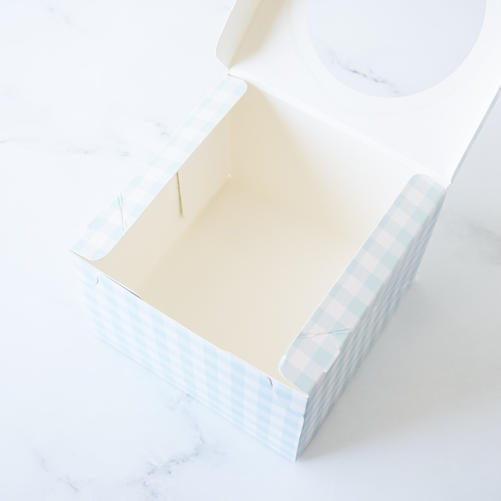 An open, empty, square gift box with a light blue and white checkered pattern. The box has a clear plastic window on the top.