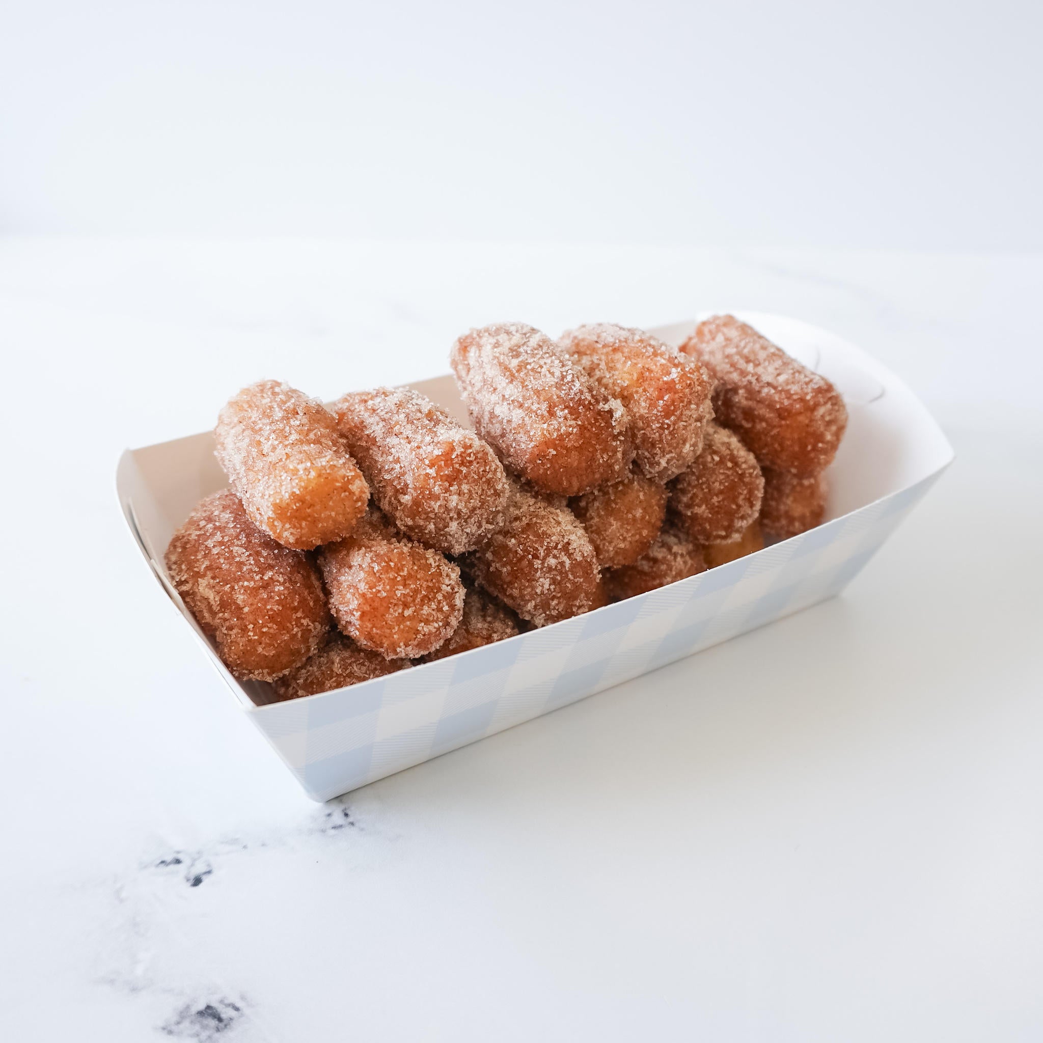 A white and blue checkered paper container filled with a stack of golden brown, sugar-coated churros.