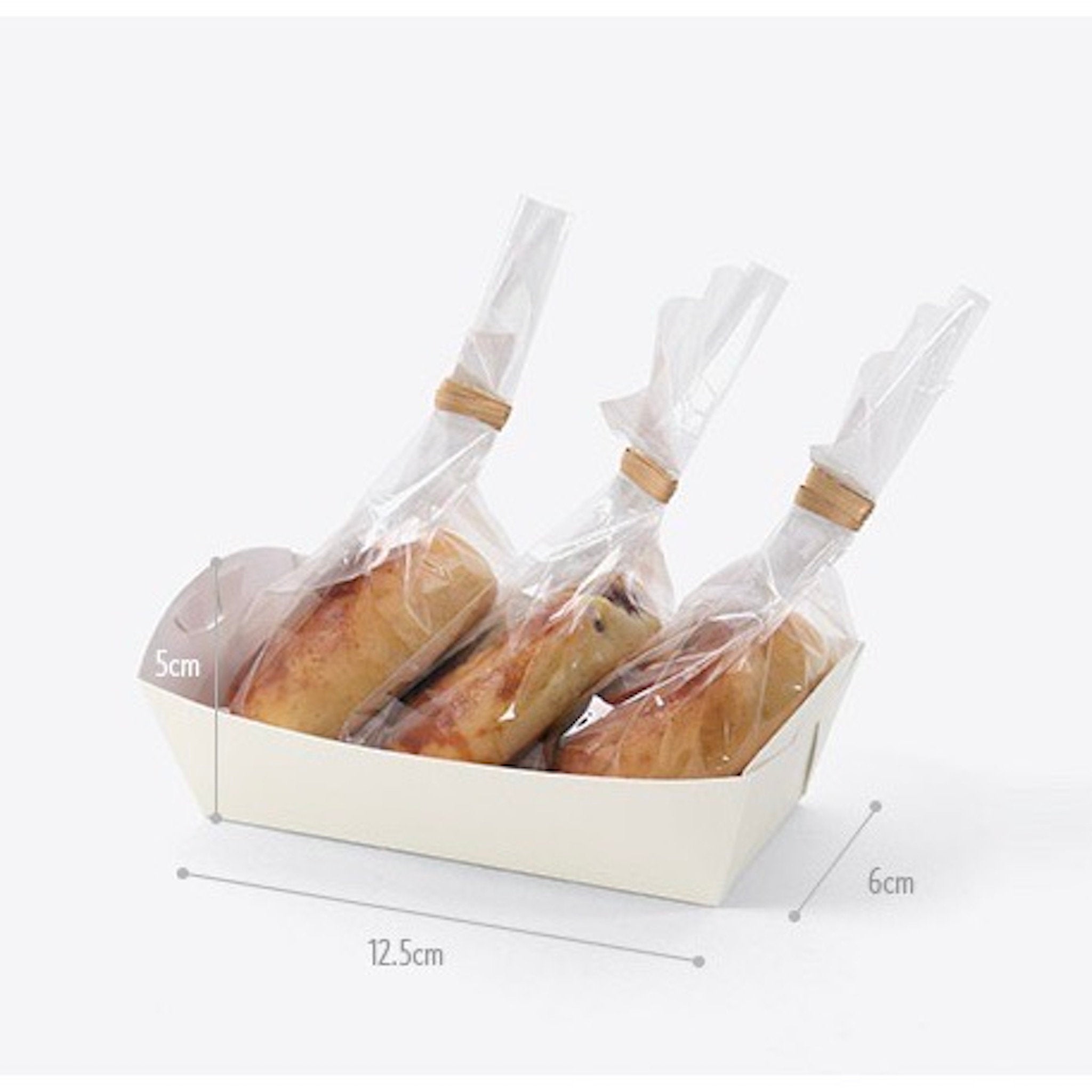 White paper food container with three clear plastic bags containing baked goods. The bags are tied with brown string. The container is 12.5cm long, 6cm wide, and 5cm high.