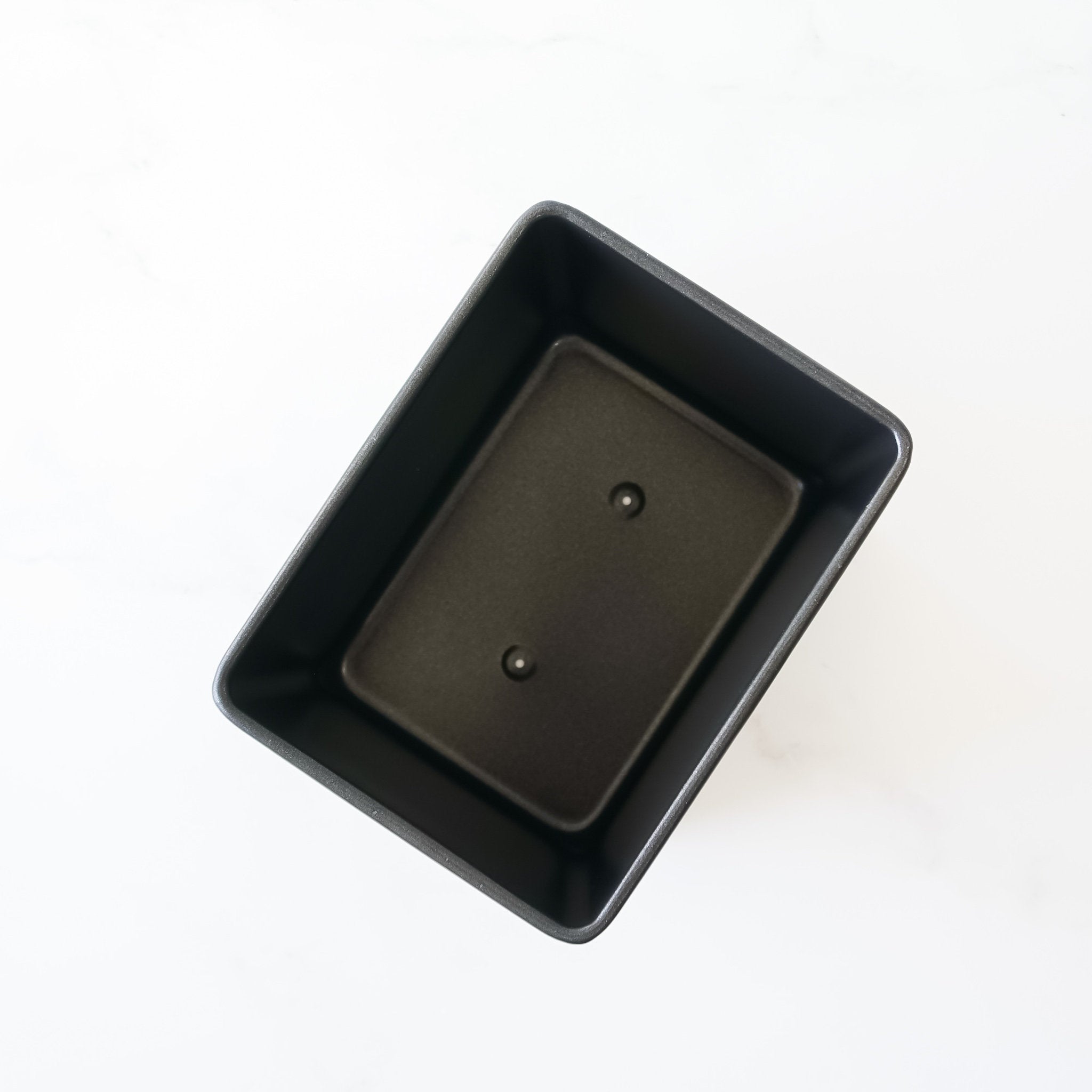 A black rectangular loaf pan with two small holes in the bottom.