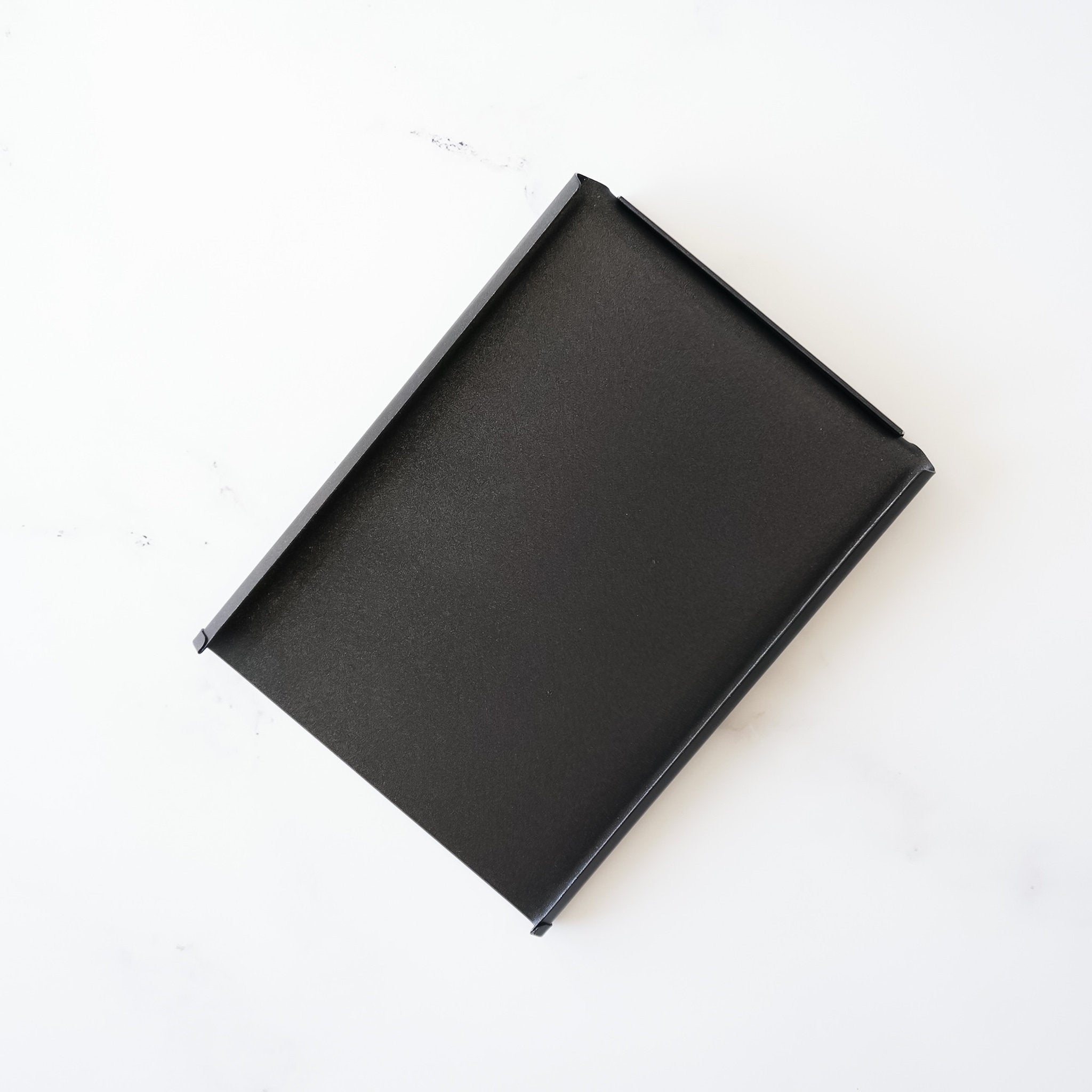 A black rectangular lid with a slightly curved edge.