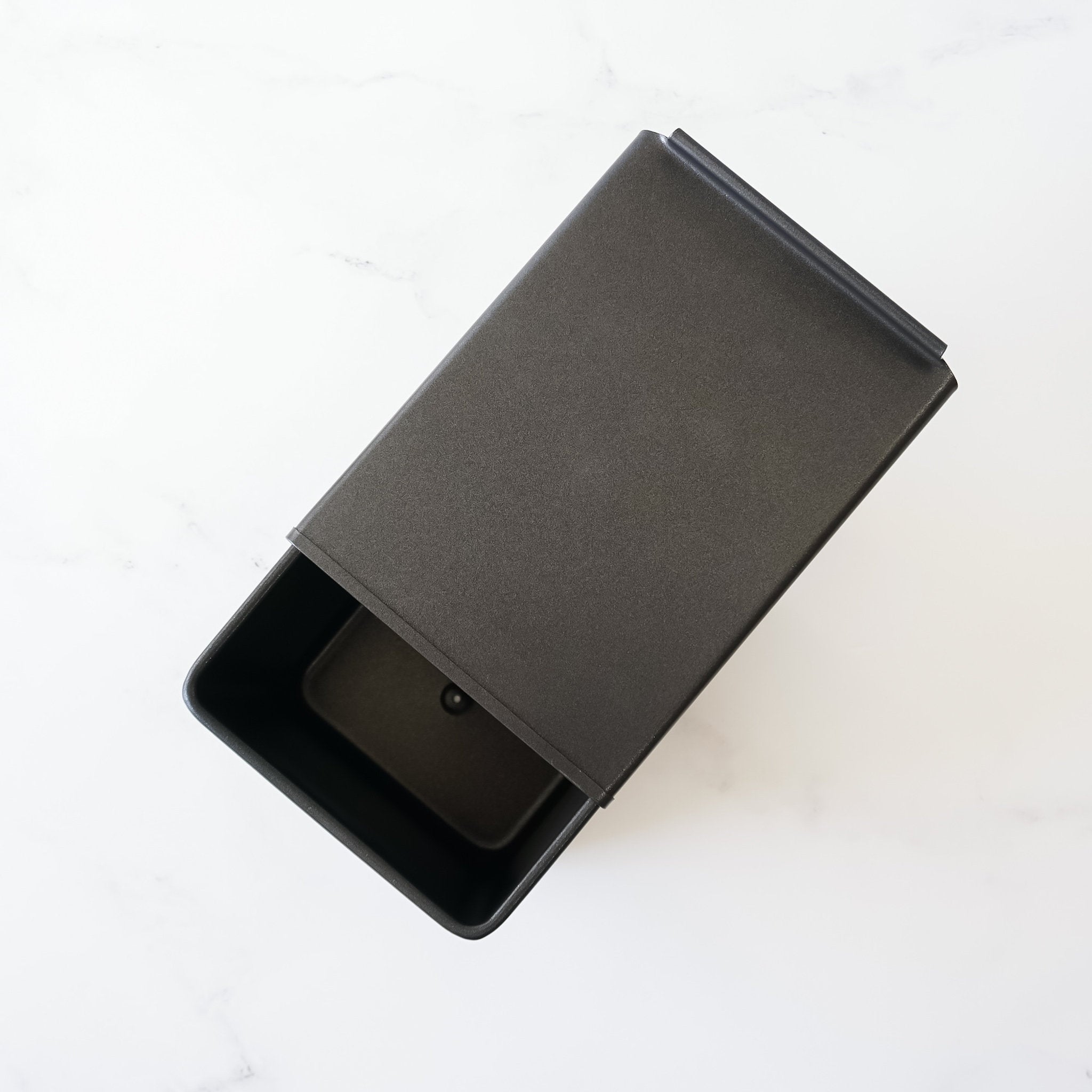 A black rectangular container with a lid. The lid is open and the container is empty.