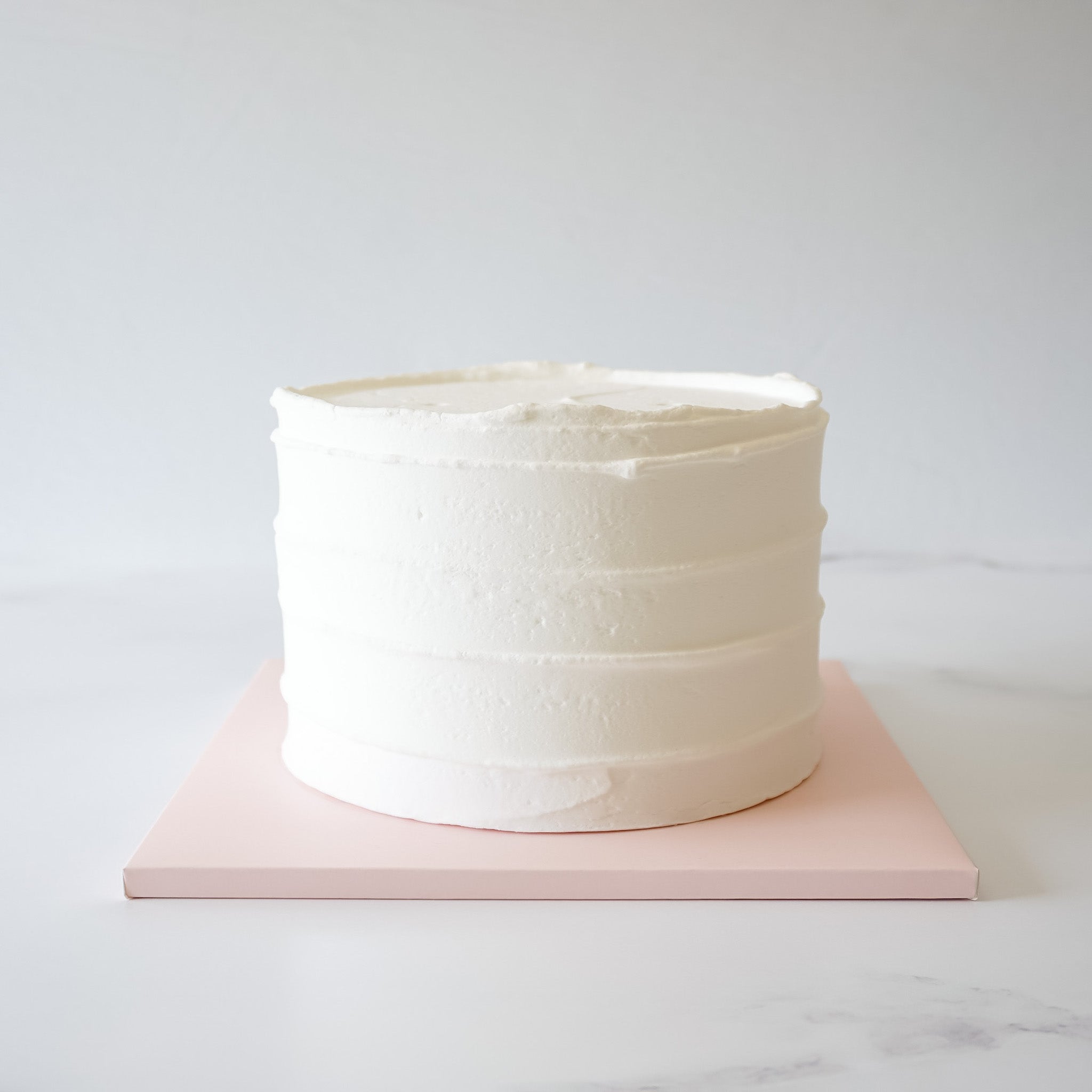 A blush pink cake board with a matte finish, displaying a frosted cake.