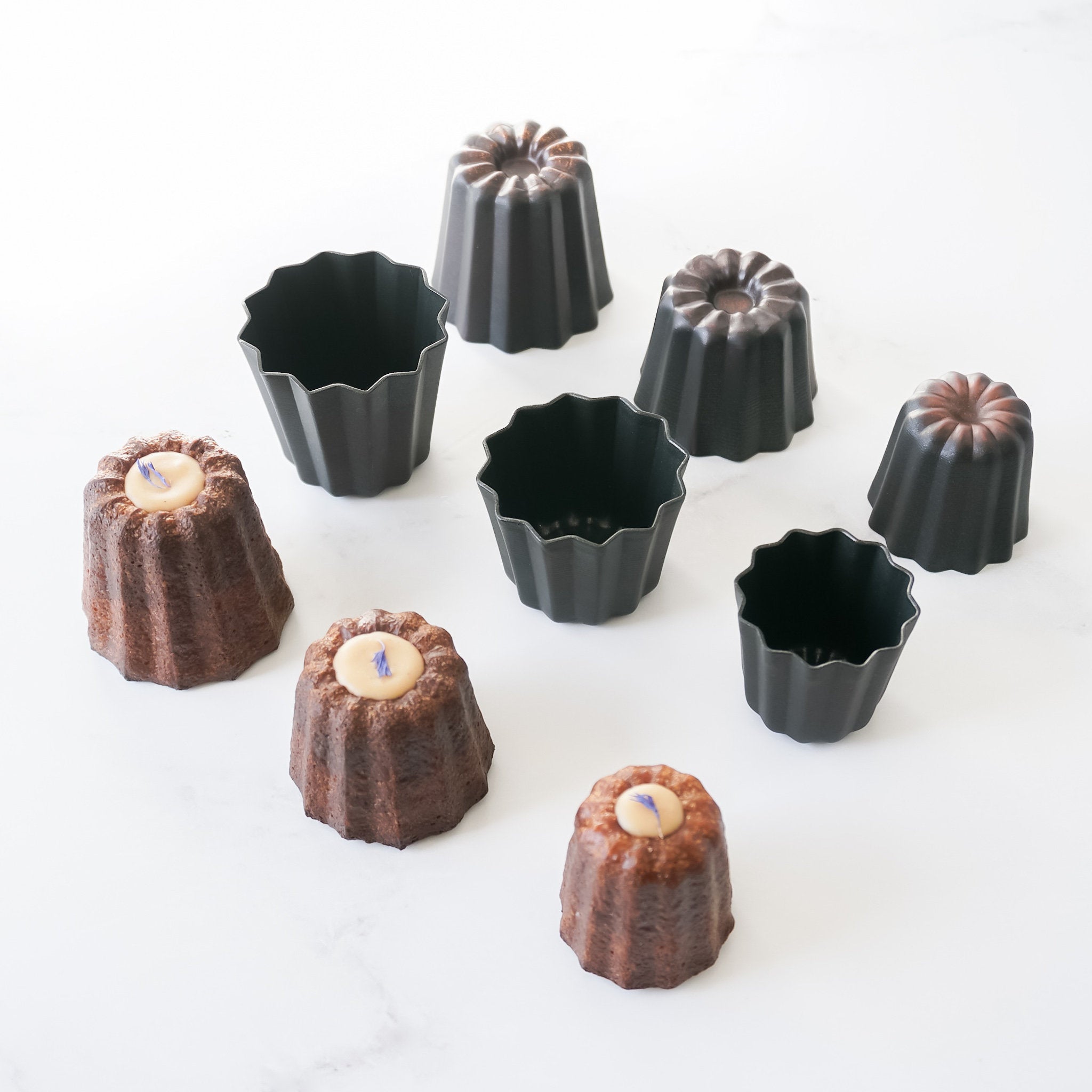 A set of individual canele molds in various sizes with a nonstick-coated copper interior, displayed on a white background.