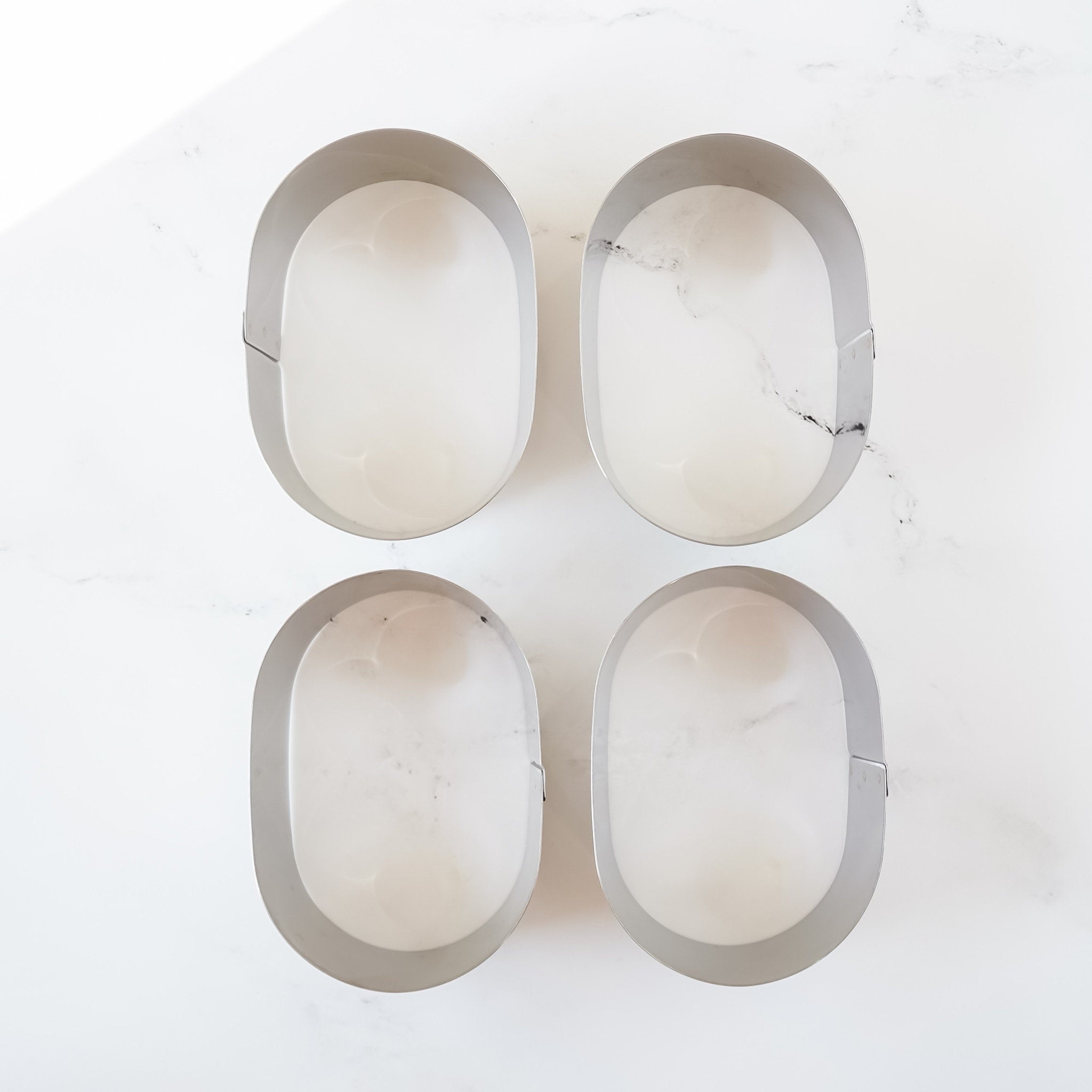 Four oval-shaped castella cake rings on a white marble surface.
