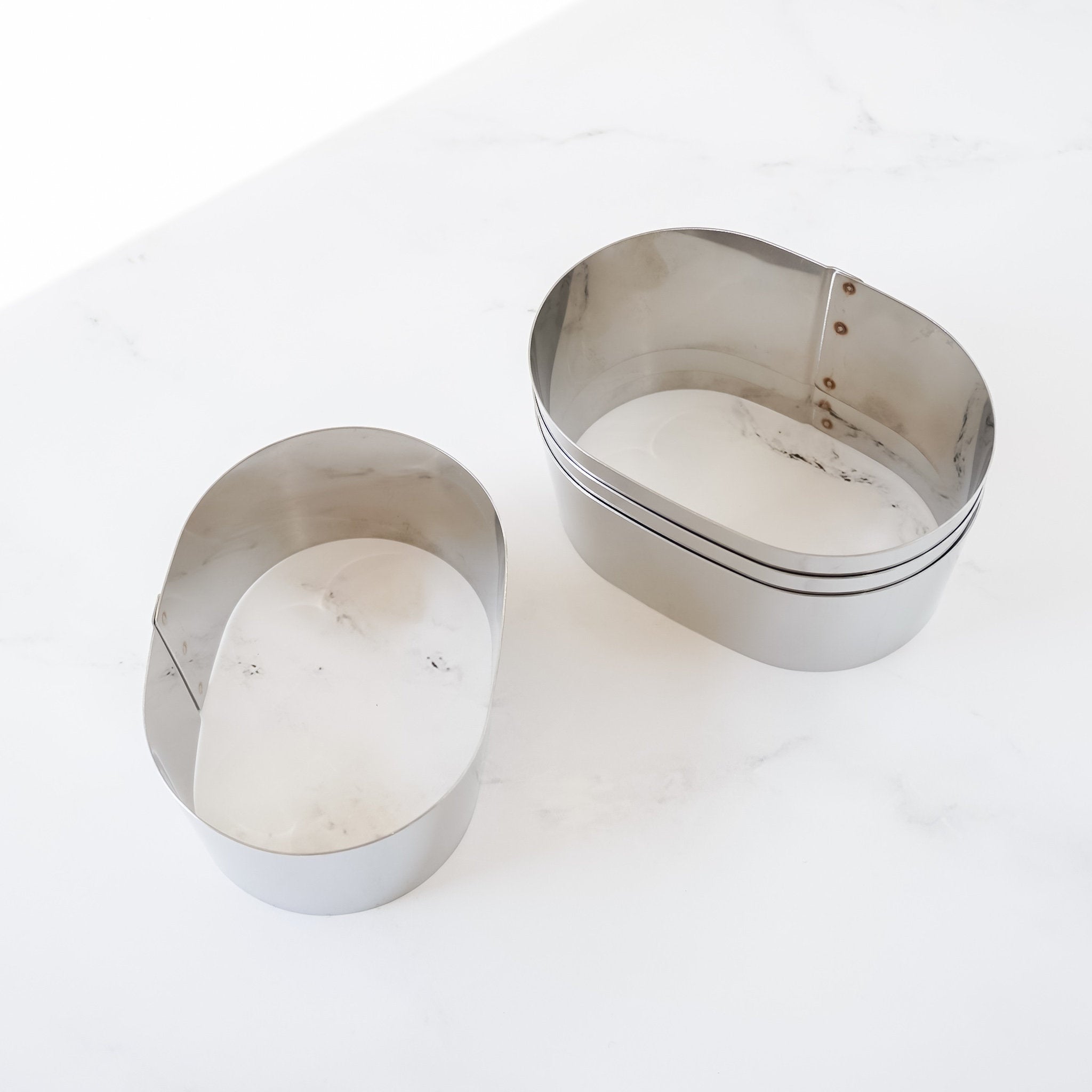Four oval-shaped castella cake rings on a white marble surface.