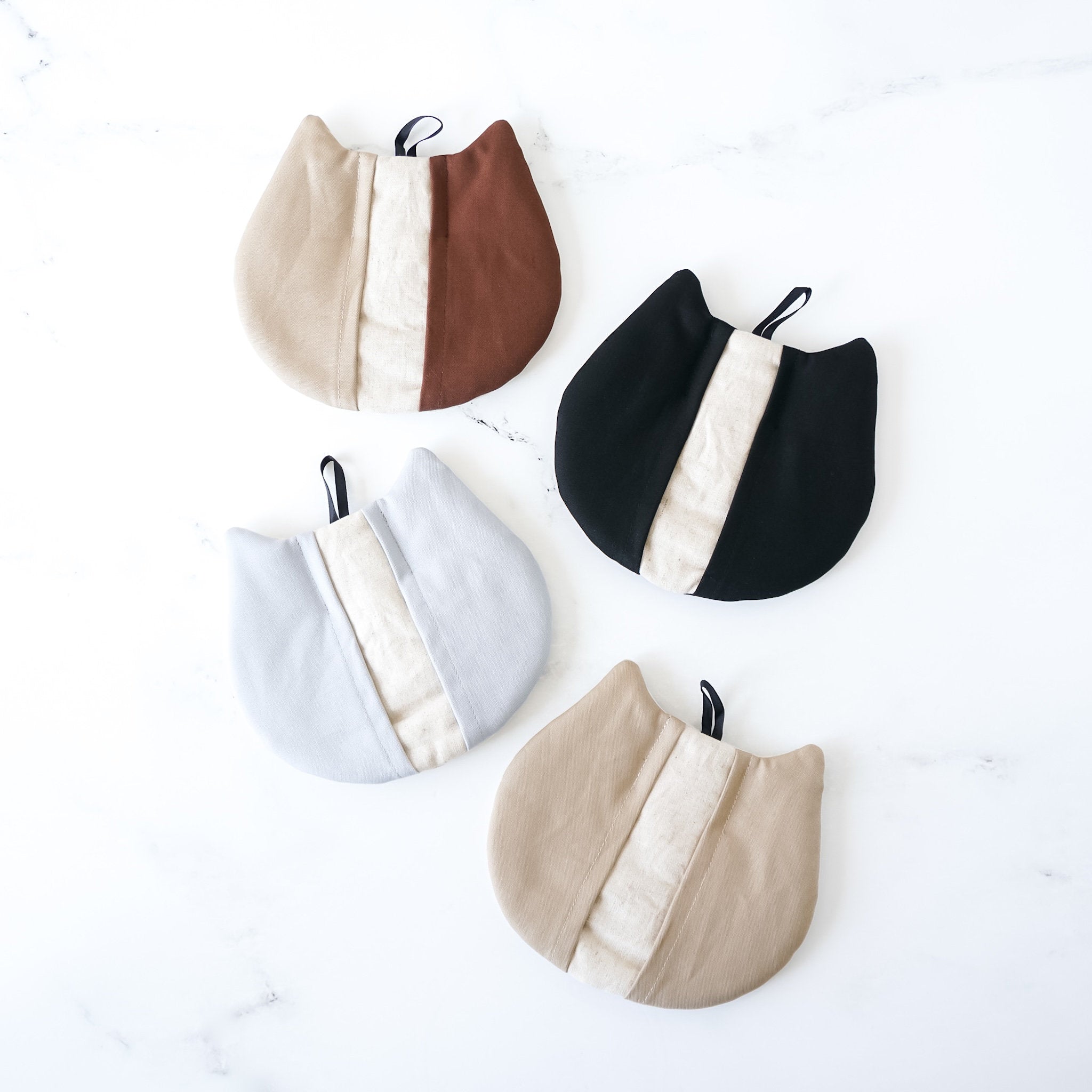 Four cat-shaped pot holders in beige, brown, black, and blue colors with a pocket-like design and a hanging loop.