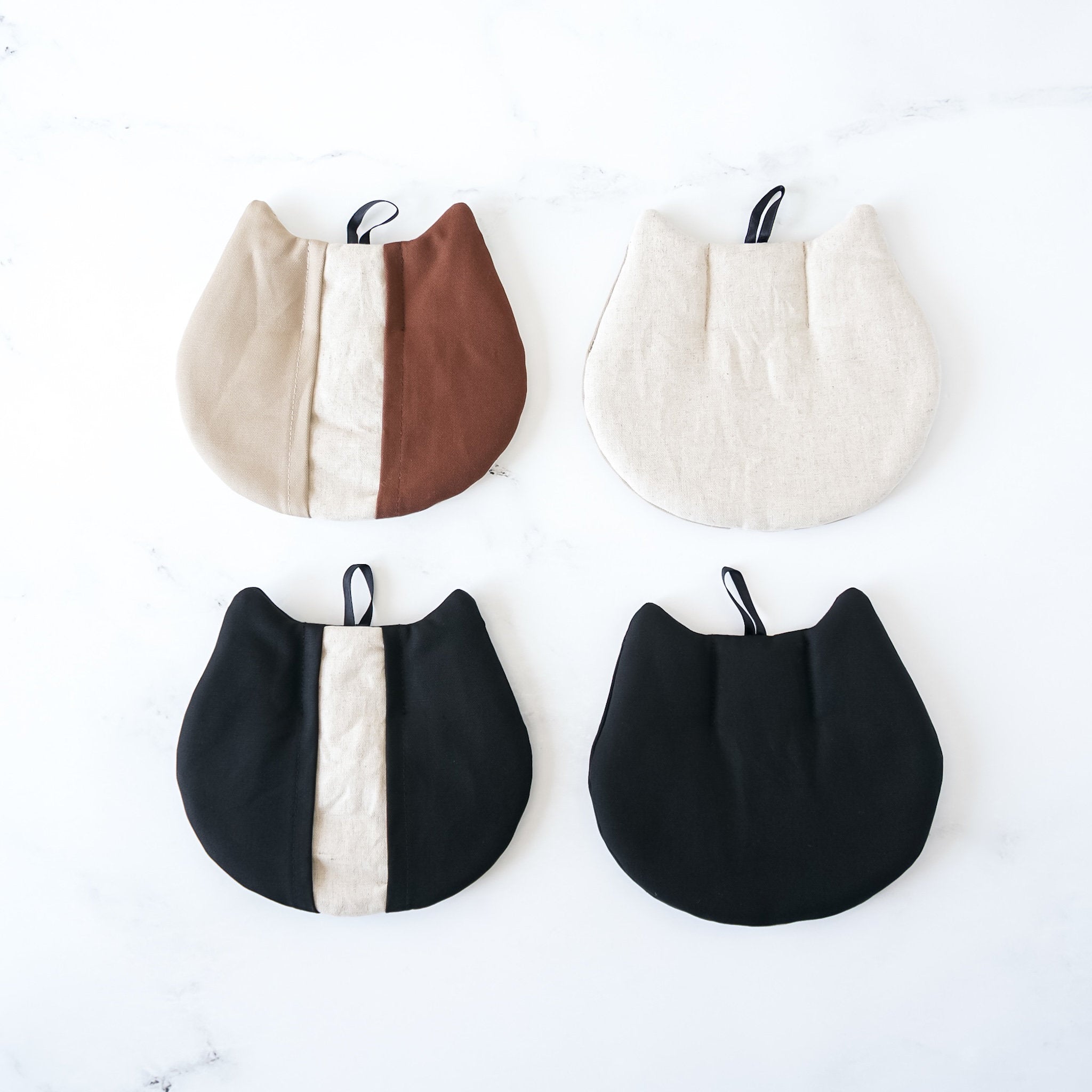 Four cat-shaped pot holders in beige, brown, black, and white colors with a pocket-like design and a hanging loop.