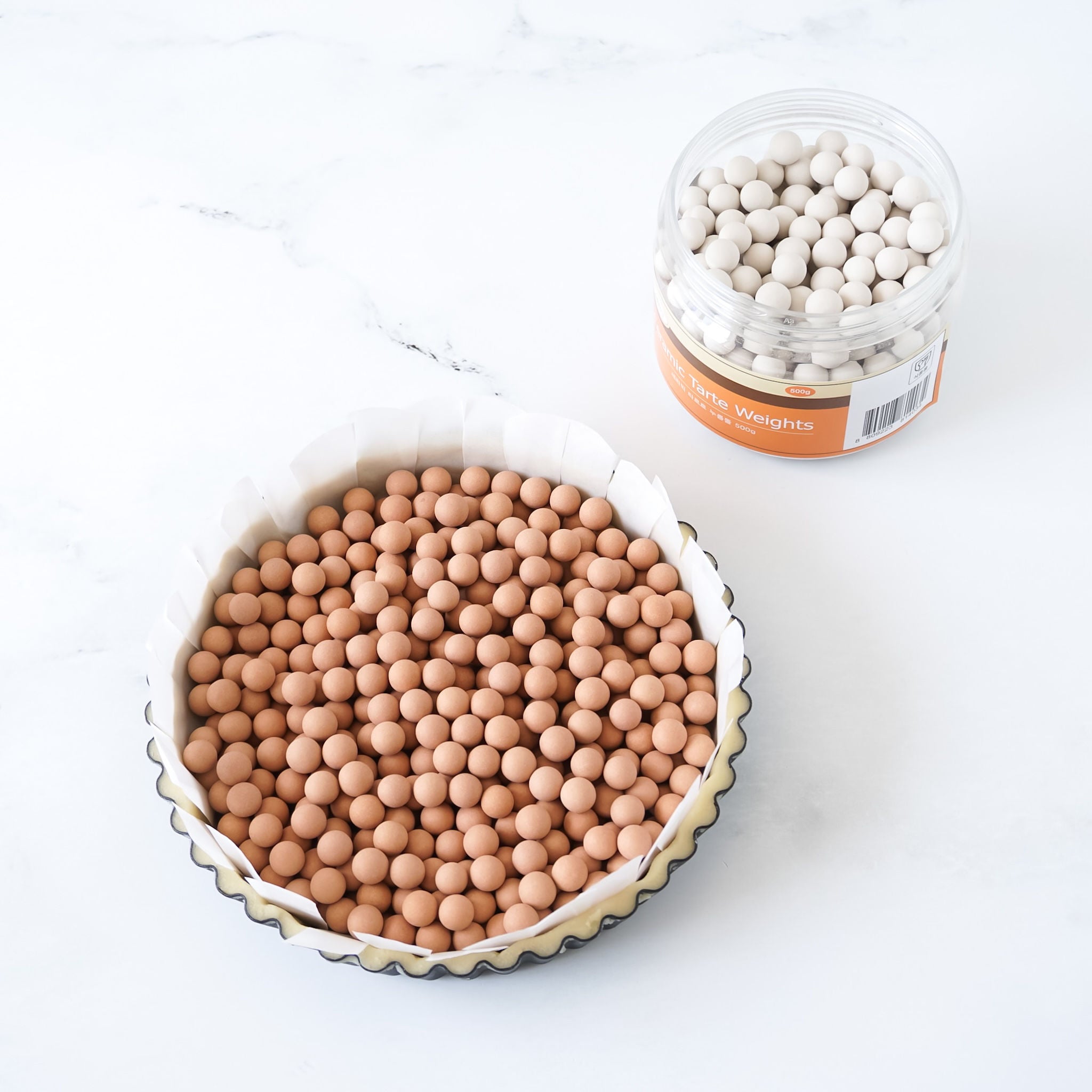 Two containers filled with ceramic pie weights on a white background