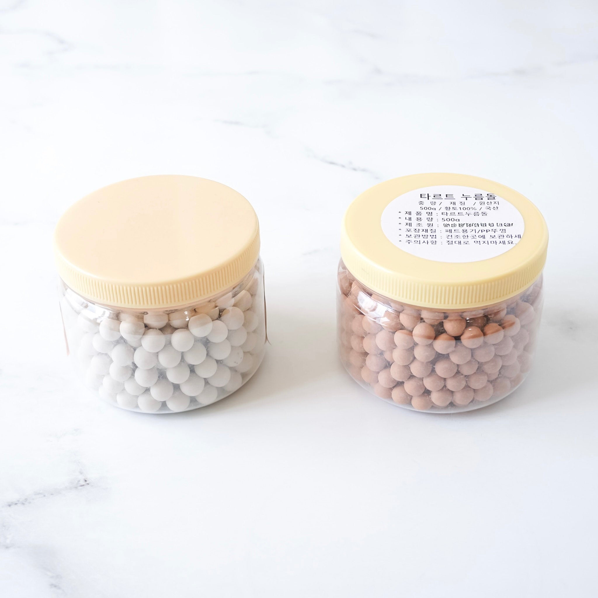 Two jars with beige lids containing white and red clay pie weights on a white background