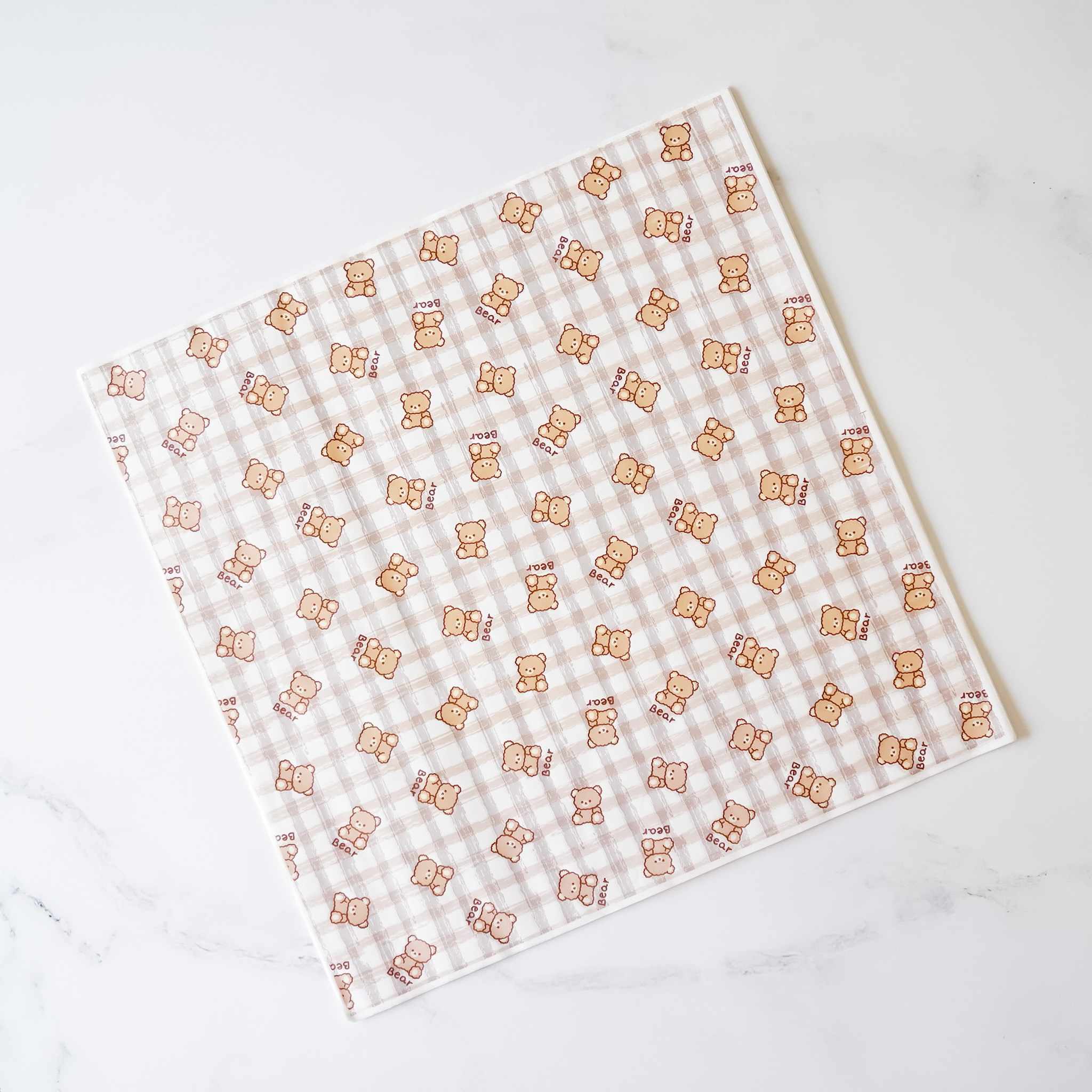 A white and brown checkered food wrapping paper with a repeating pattern of brown teddy bears. The bears are wearing bows and have the word &