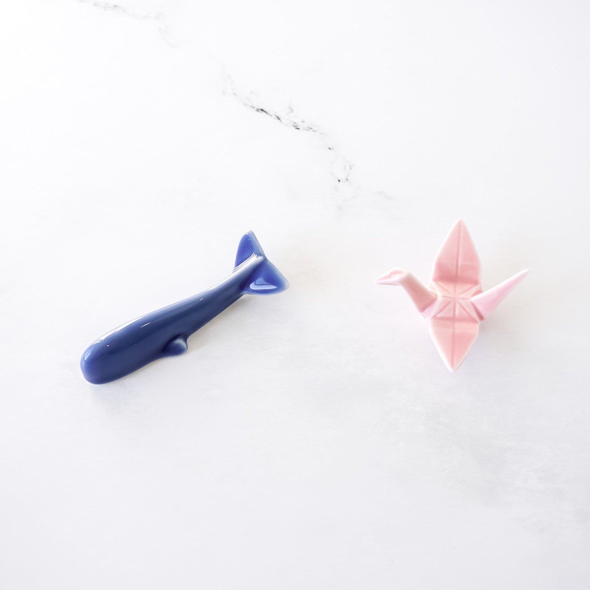 Blue whale and pink origami crane chopstick rests on a white background