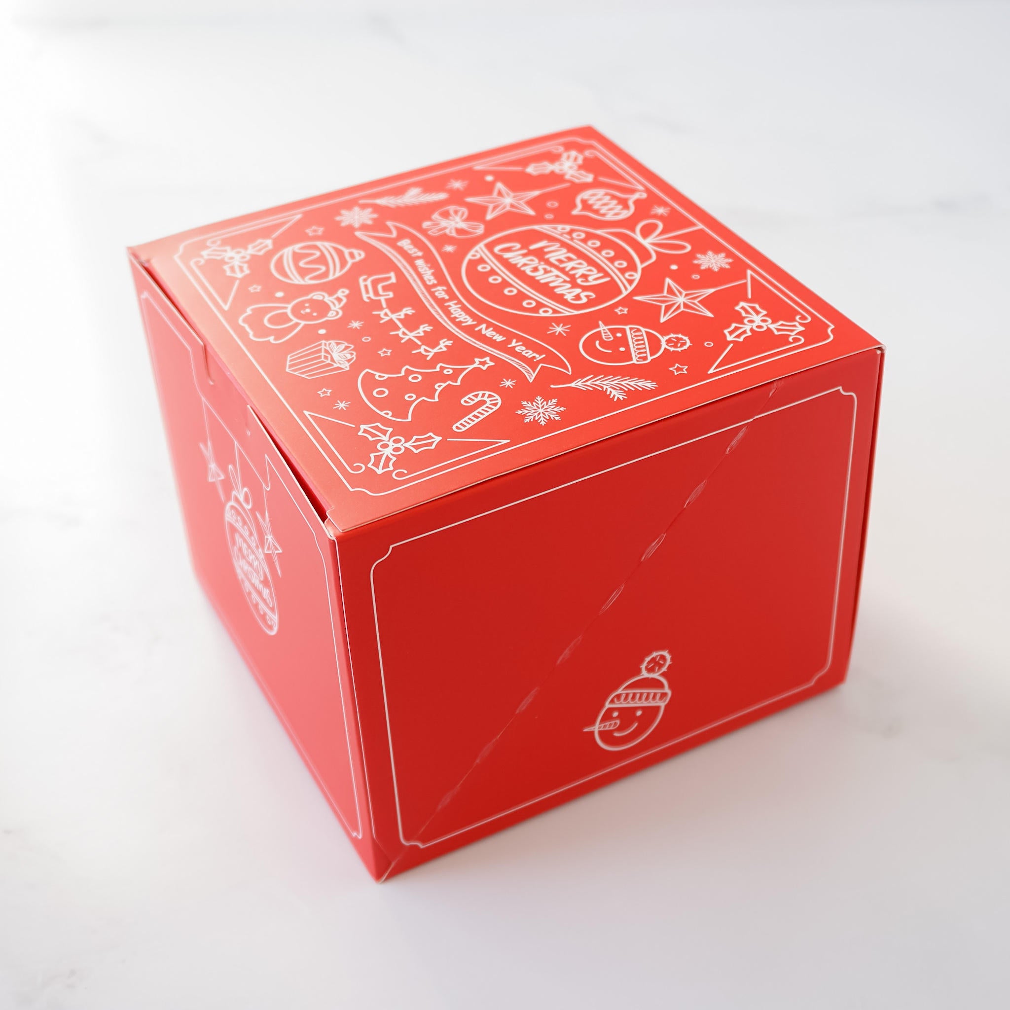 A red square Christmas gift box features a white line drawing design of various Christmas icons and the text &
