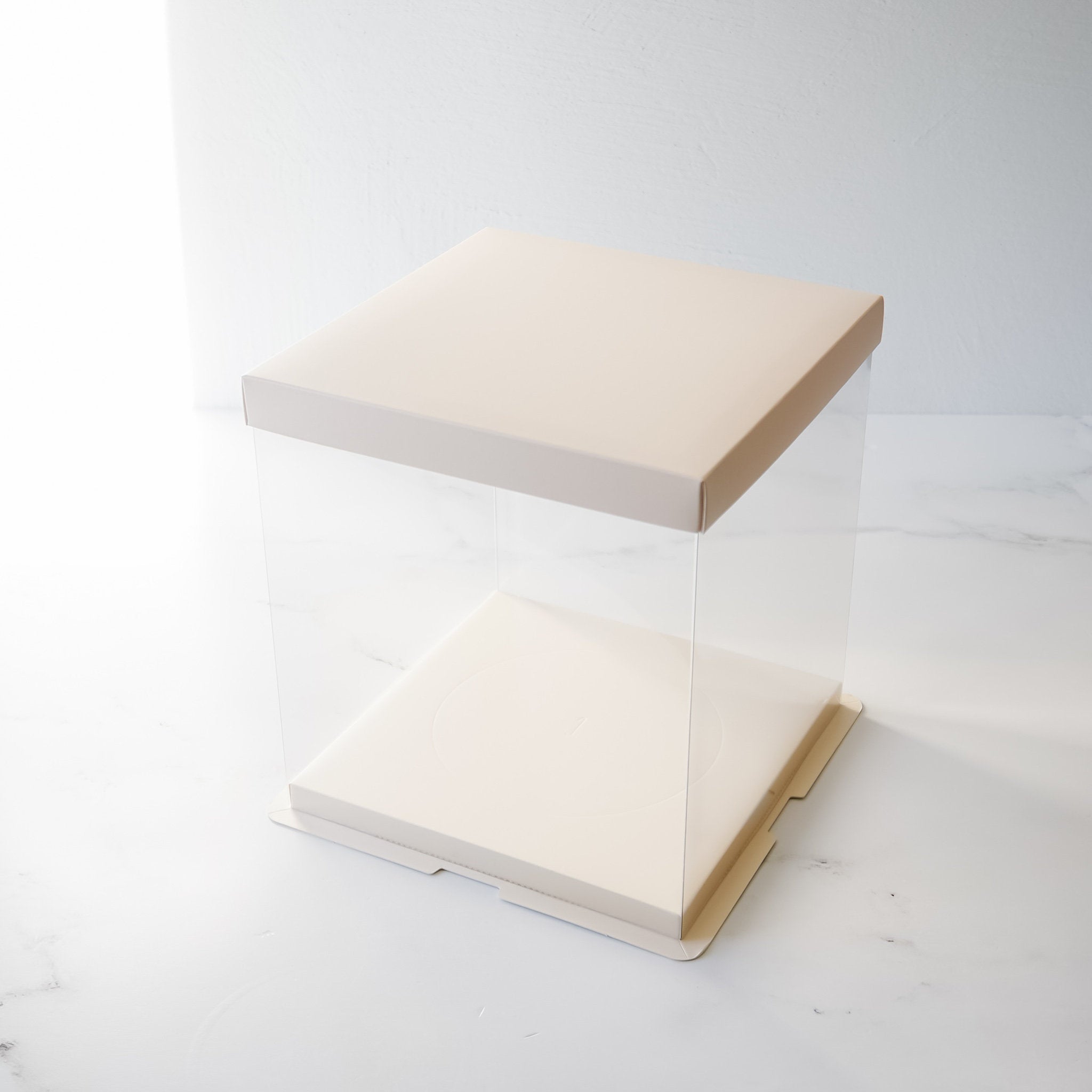 A clear plastic cake box with a white cardboard lid and base. The box is empty and ready to be filled with a cake.