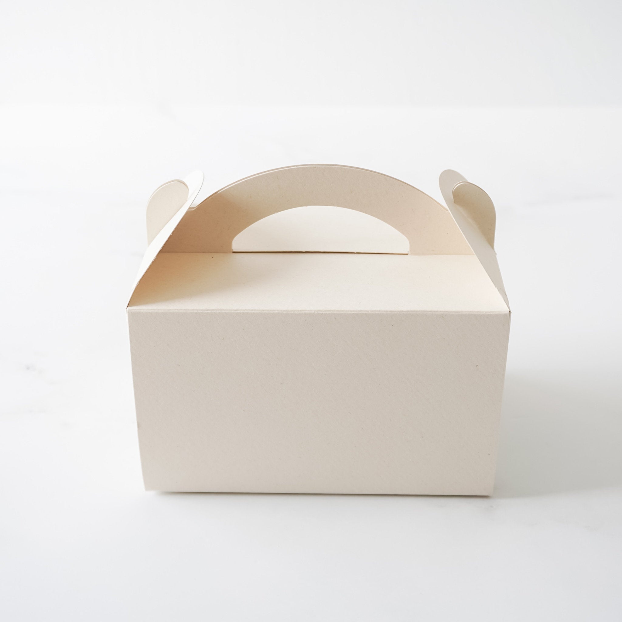 A light beige cardboard box with a cut-out handle. The box is empty and has a smooth surface.