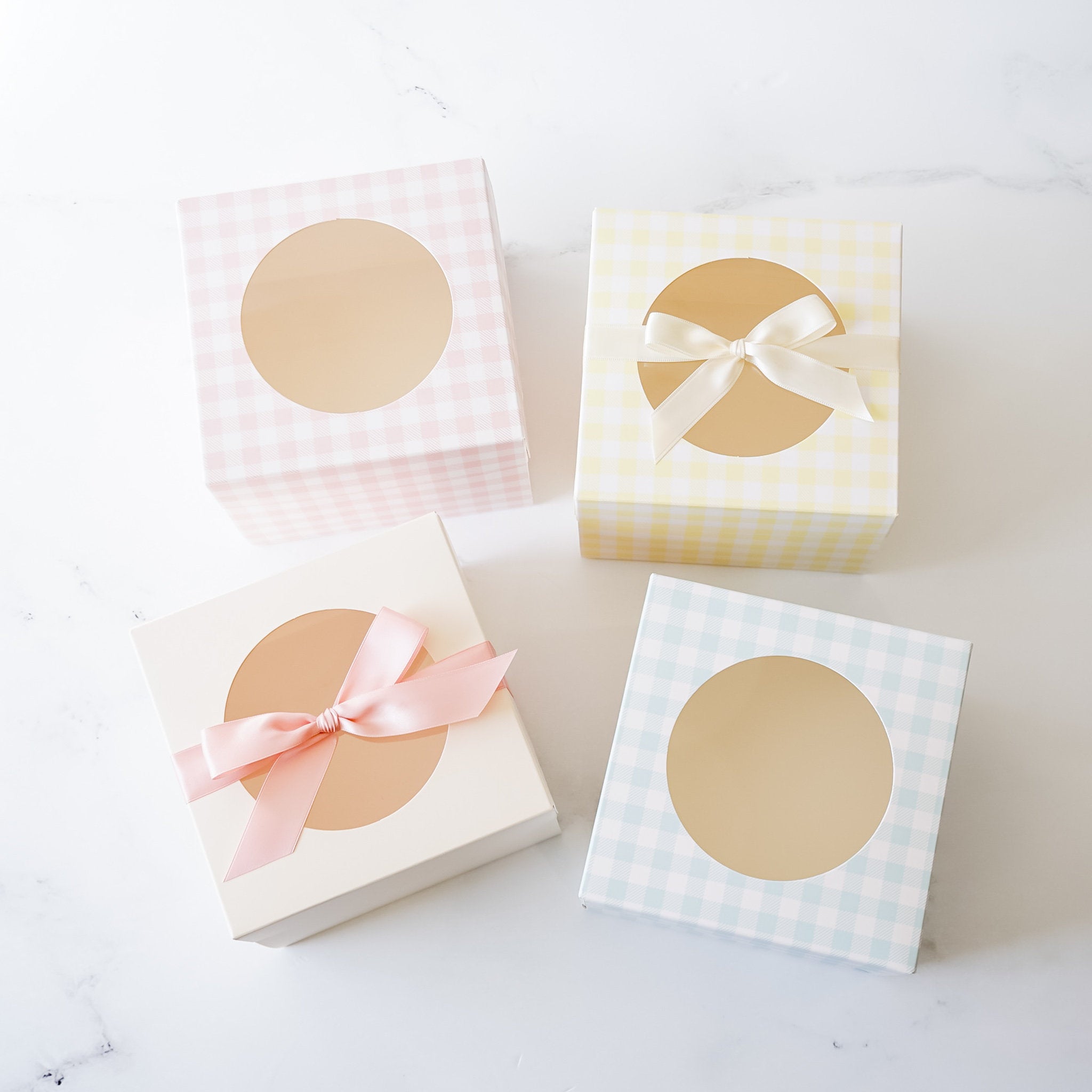 Four square gift boxes with a window and a ribbon. The boxes are in pink, yellow, white, and blue gingham patterns.