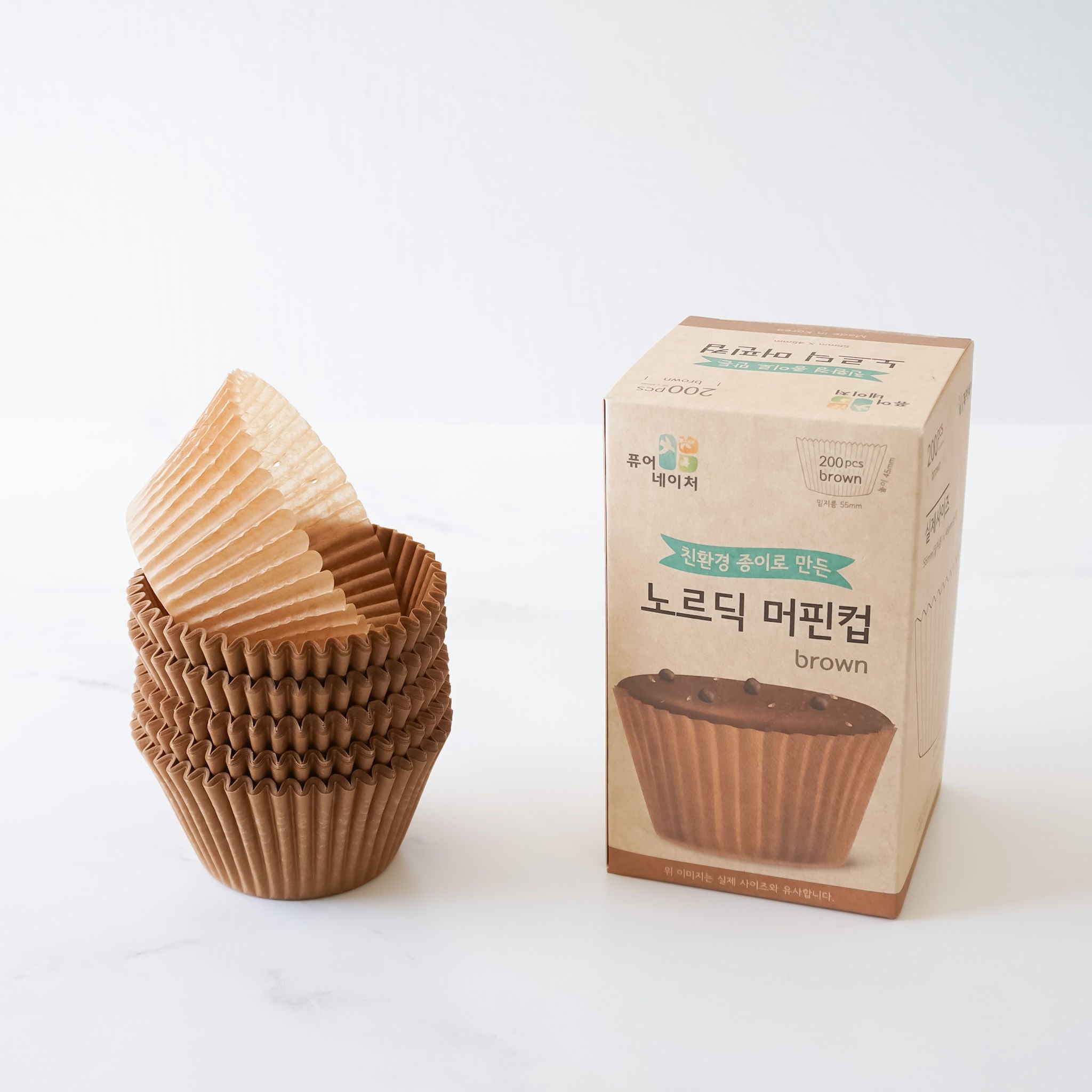 A stack of brown paper cupcake liners. The liners are fluted and have a slight sheen. The liners are next to a box of brown parchment paper cupcake liners.