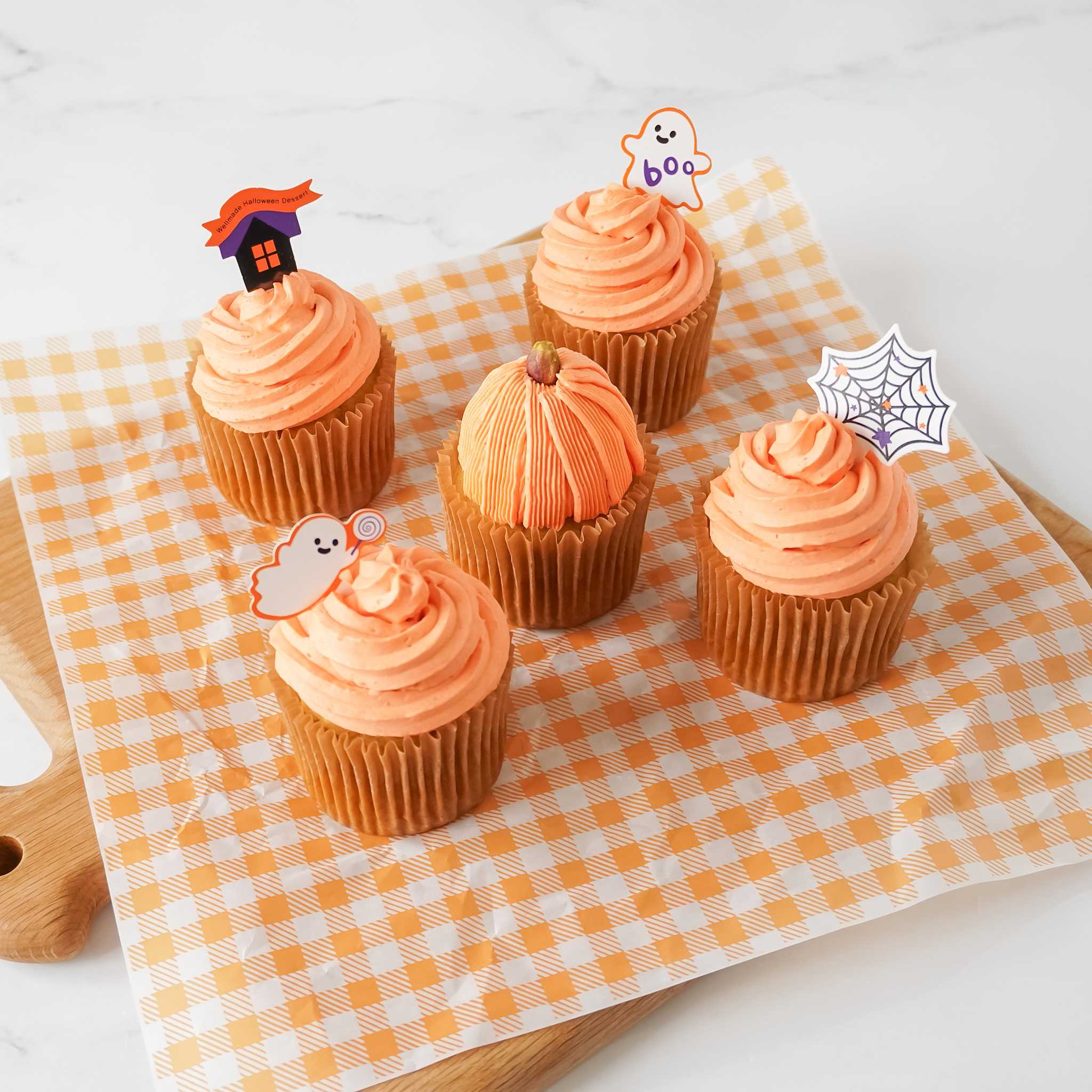 A set of Halloween-themed cupcake toppers placed on top of cupcakes, with designs including a witch, a pumpkin, and a spider web on a checkered background.