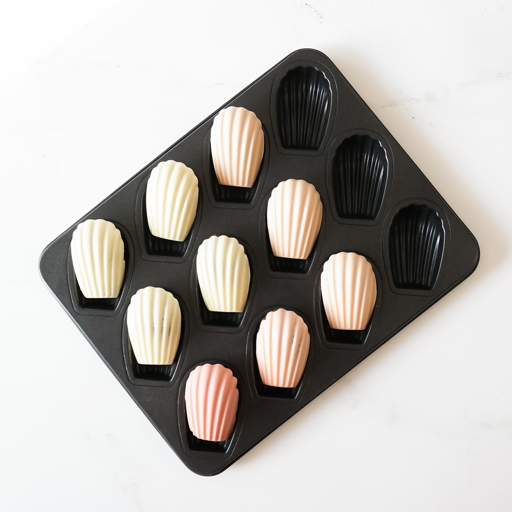 A nonstick deep Madeleine pan with 12 cavities, some filled with dough, others empty, on a white background.