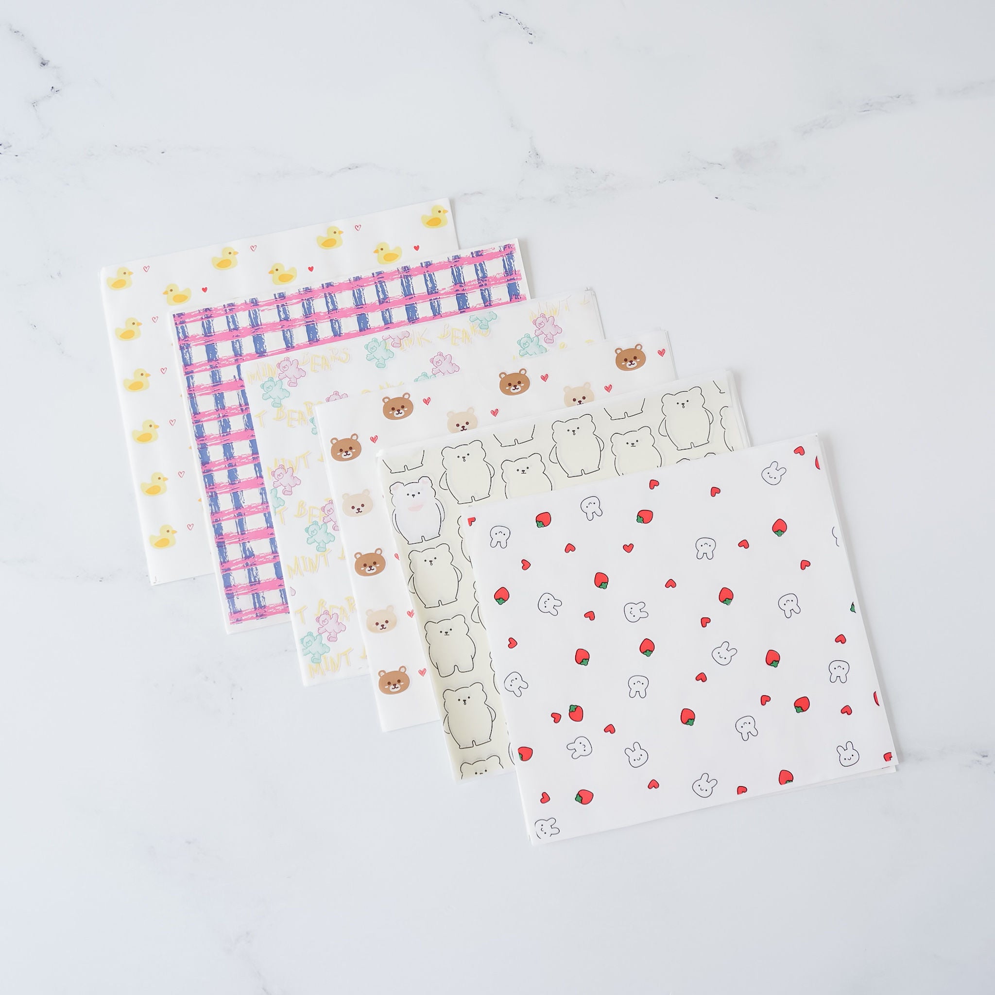 Assorted deli papers with various patterns including dots, animals, and geometric designs, displayed on a marble surface.
