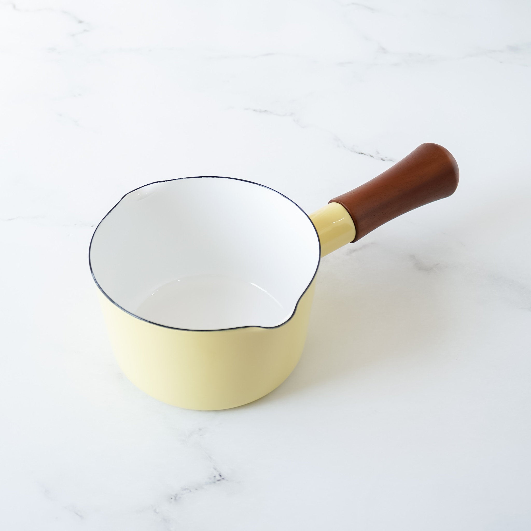 A butter yellow enamel-coated steel saucepan with a wooden handle, displayed against a marble background.