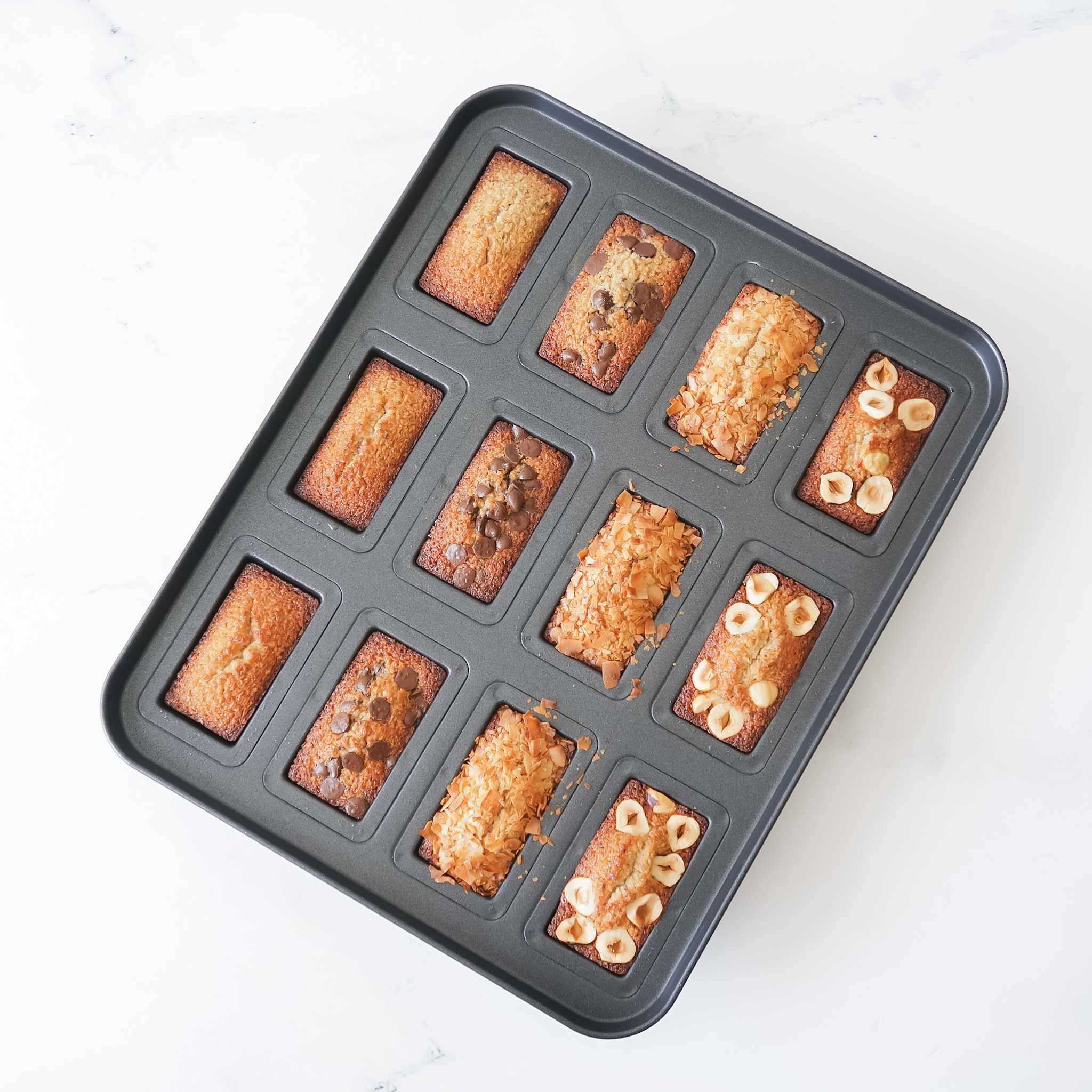 A financier cake pan with 12 cavity molds, containing freshly baked cakes with a non-stick surface.