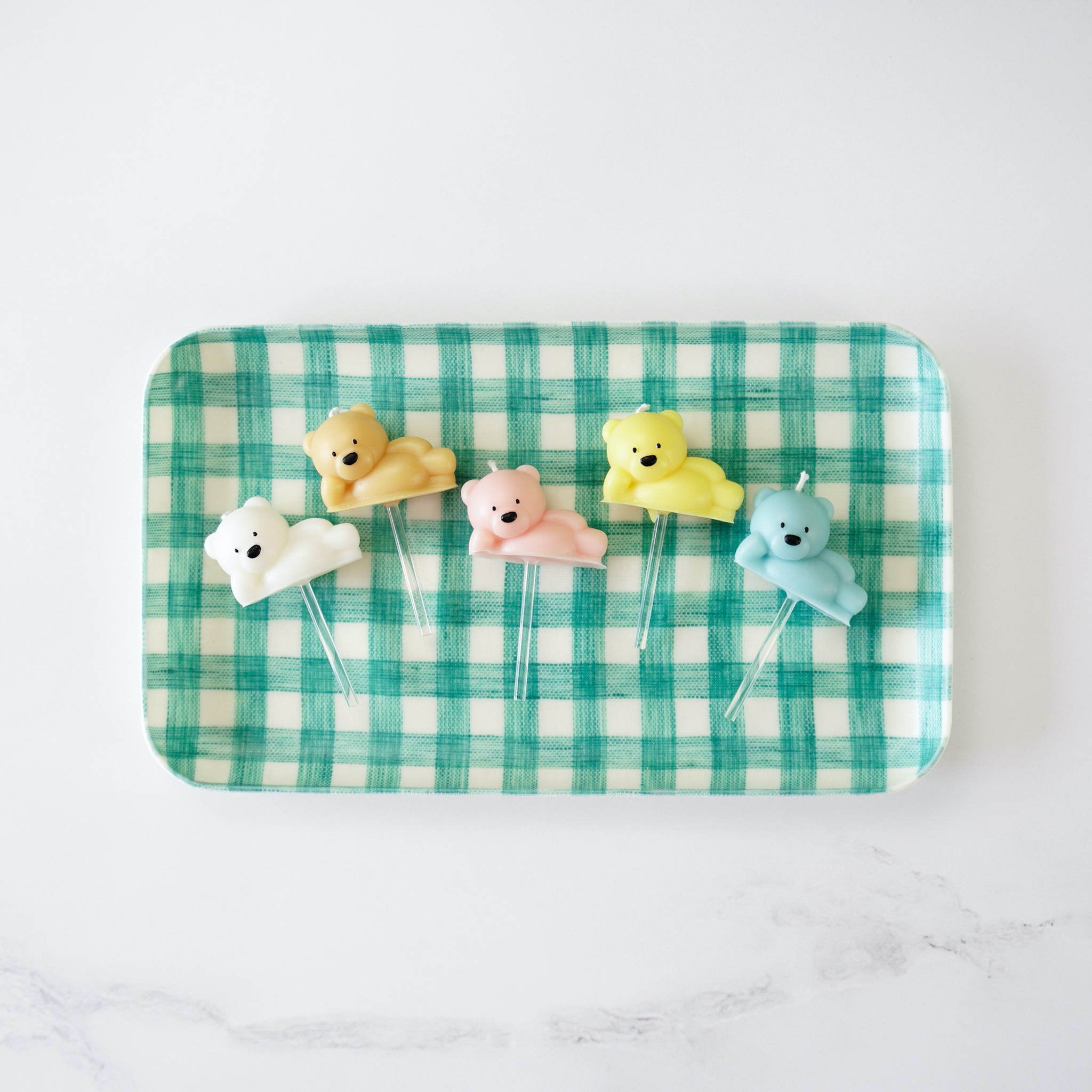 A green check linen coated tray with birthday bear candles on it, placed on a white surface.