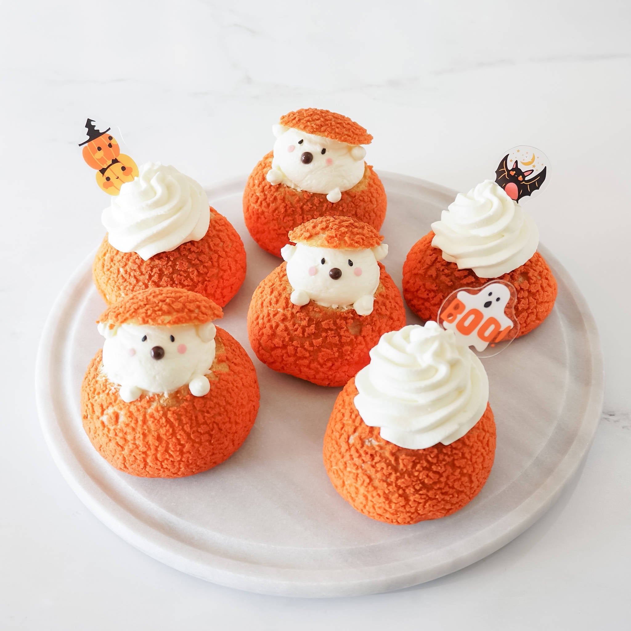A set of Halloween cupcake toppers with three designs: a pumpkin, a ghost, and a bat, displayed on a plate.
