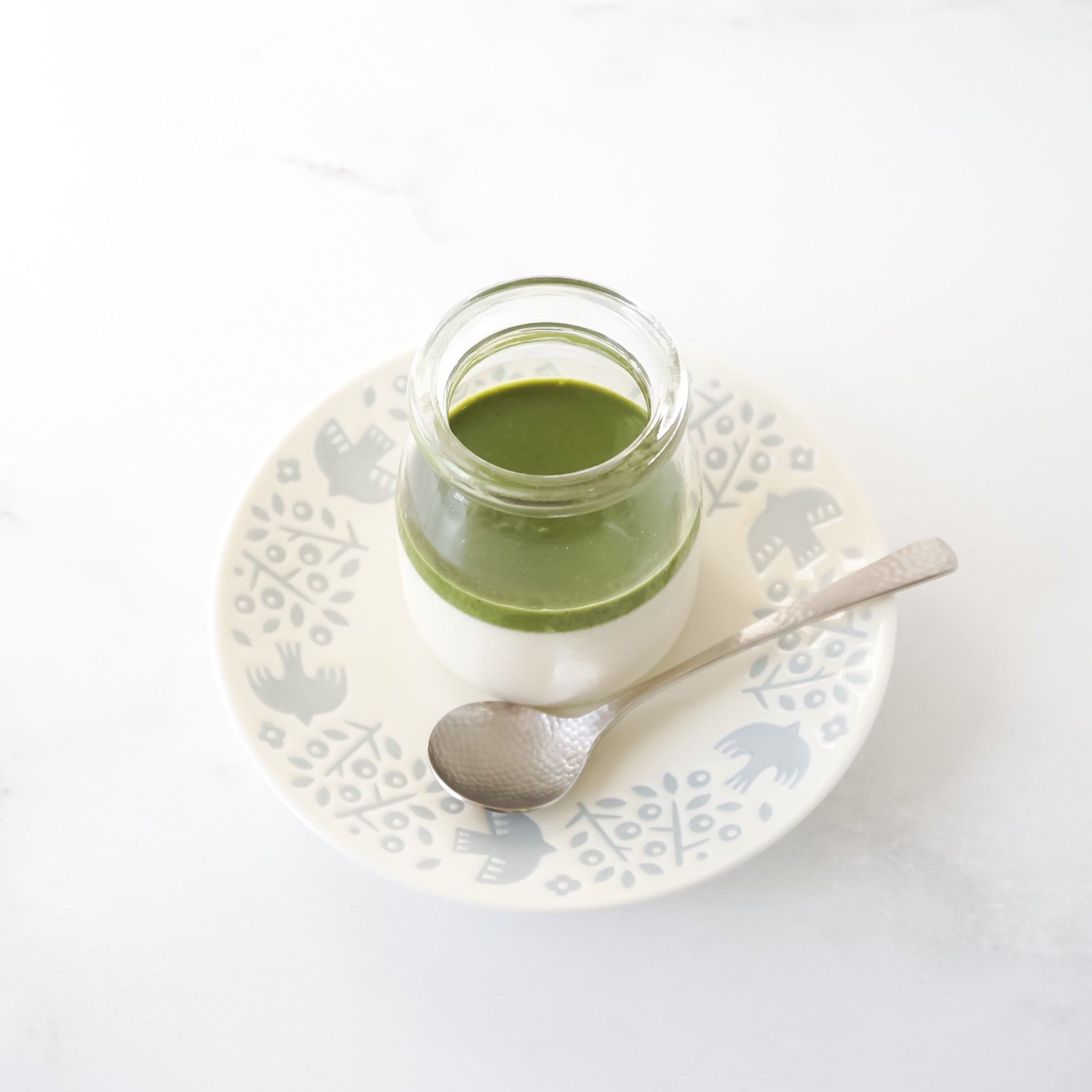 Jar of matcha panna cotta on a decorative plate with a spoon