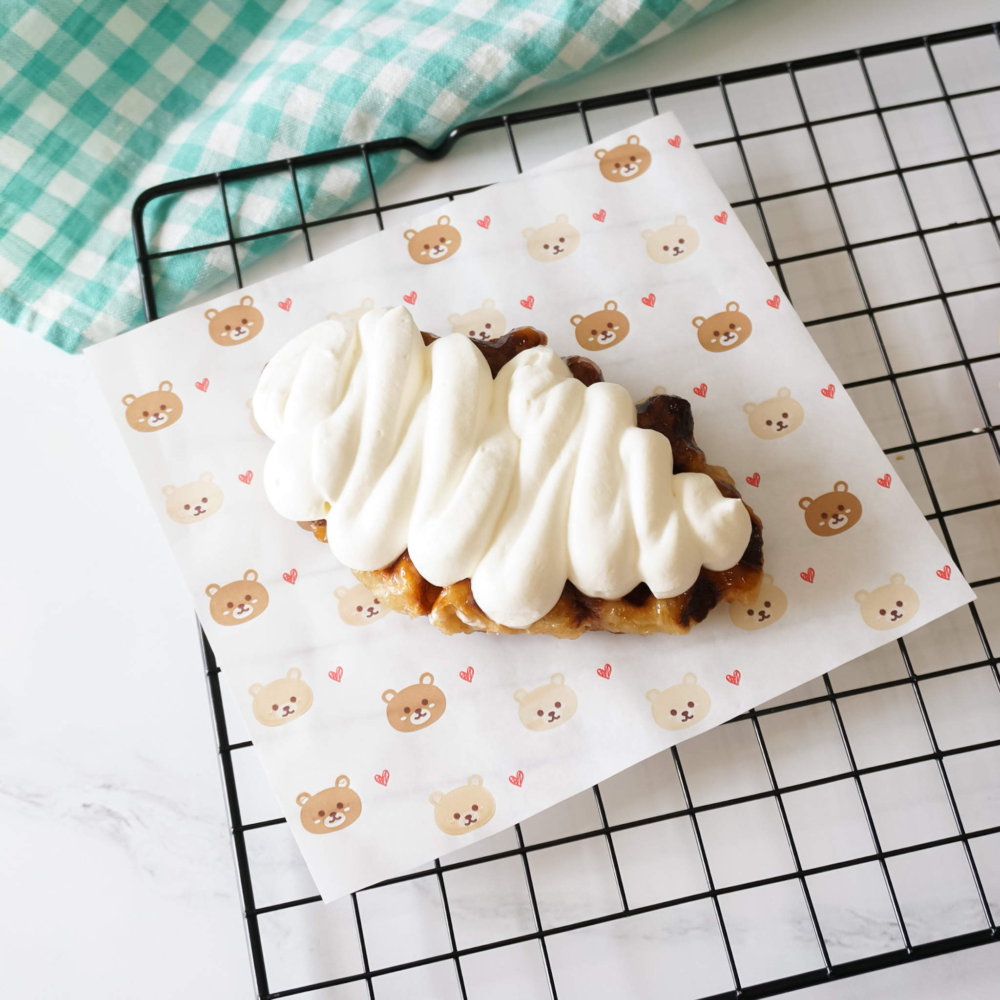 A sheet of deli paper with a bear and heart pattern, used to line a cooling rack for a pastry with frosting on top.