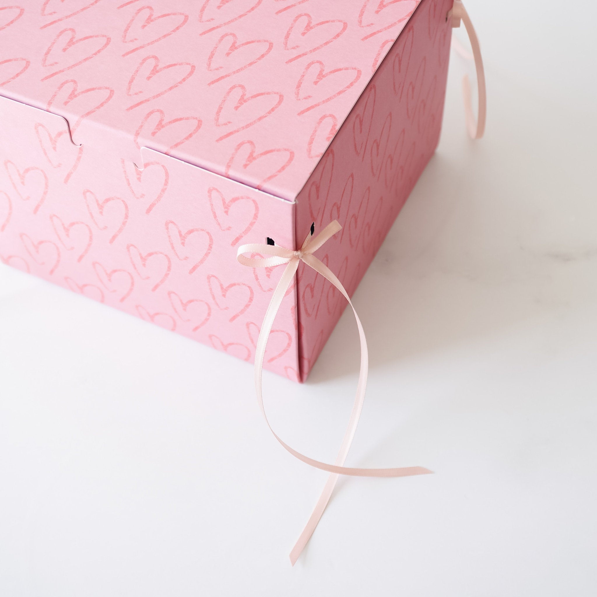 A pink gift box with a heart pattern and pink ribbon ties.