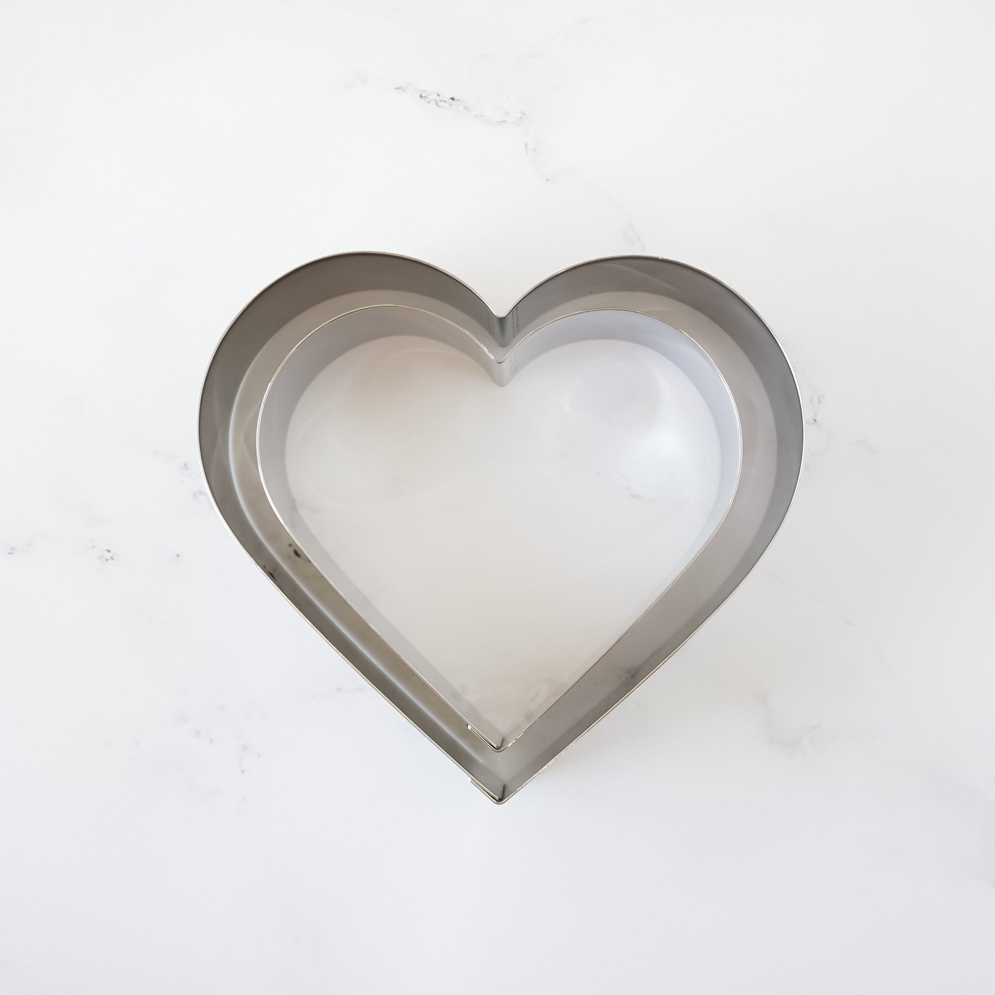 A silver heart-shaped cookie cutter with a smaller heart-shaped cookie cutter inside.