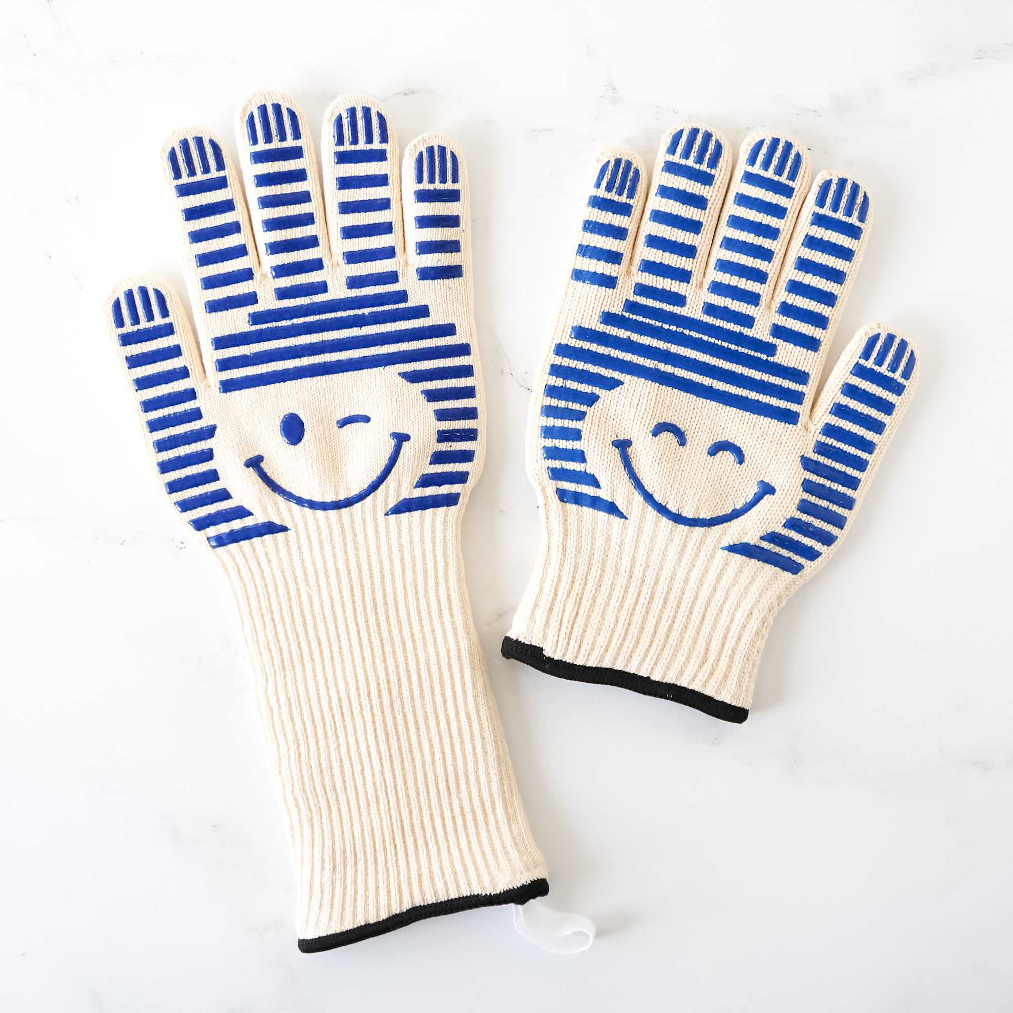 A pair of beige oven gloves with blue stripes and a smiley face design on the back.