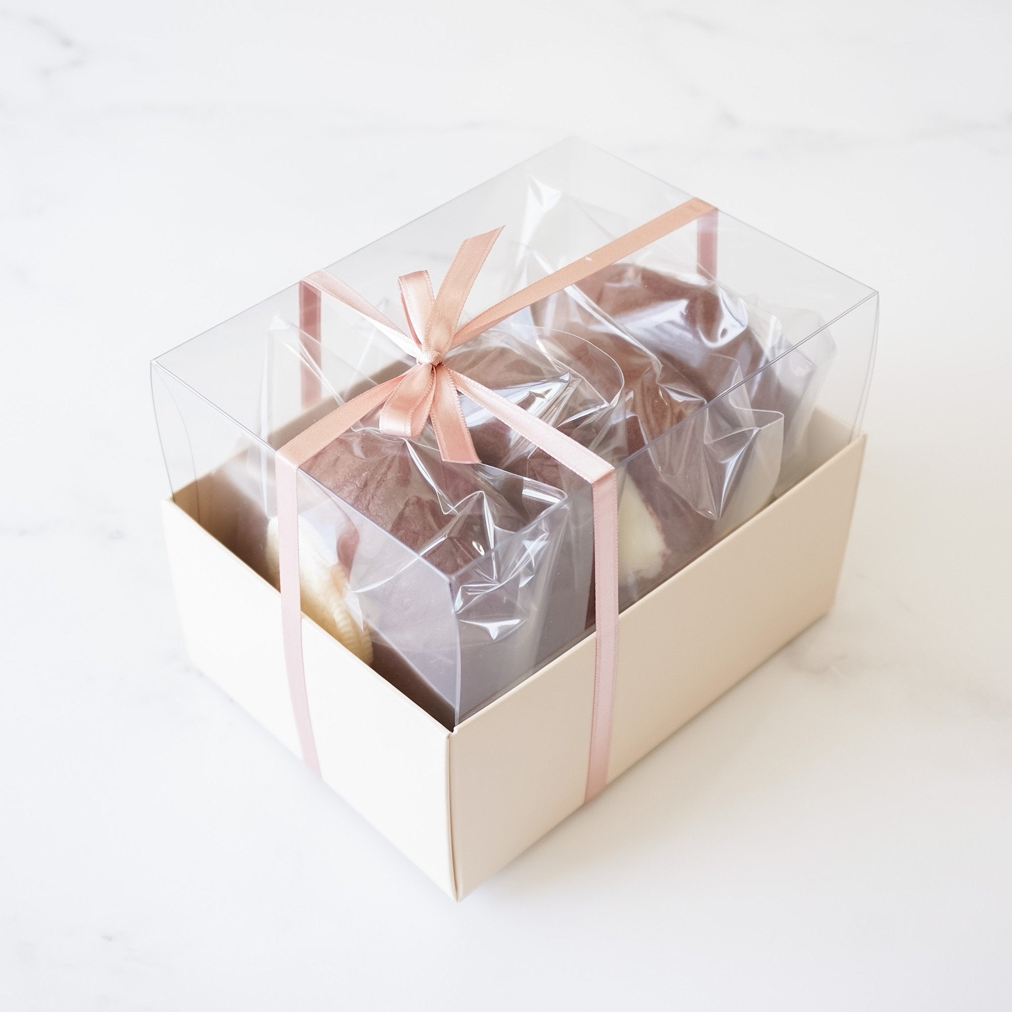Four cookies in a bakery box with a pink ribbon. The box is on a white surface.