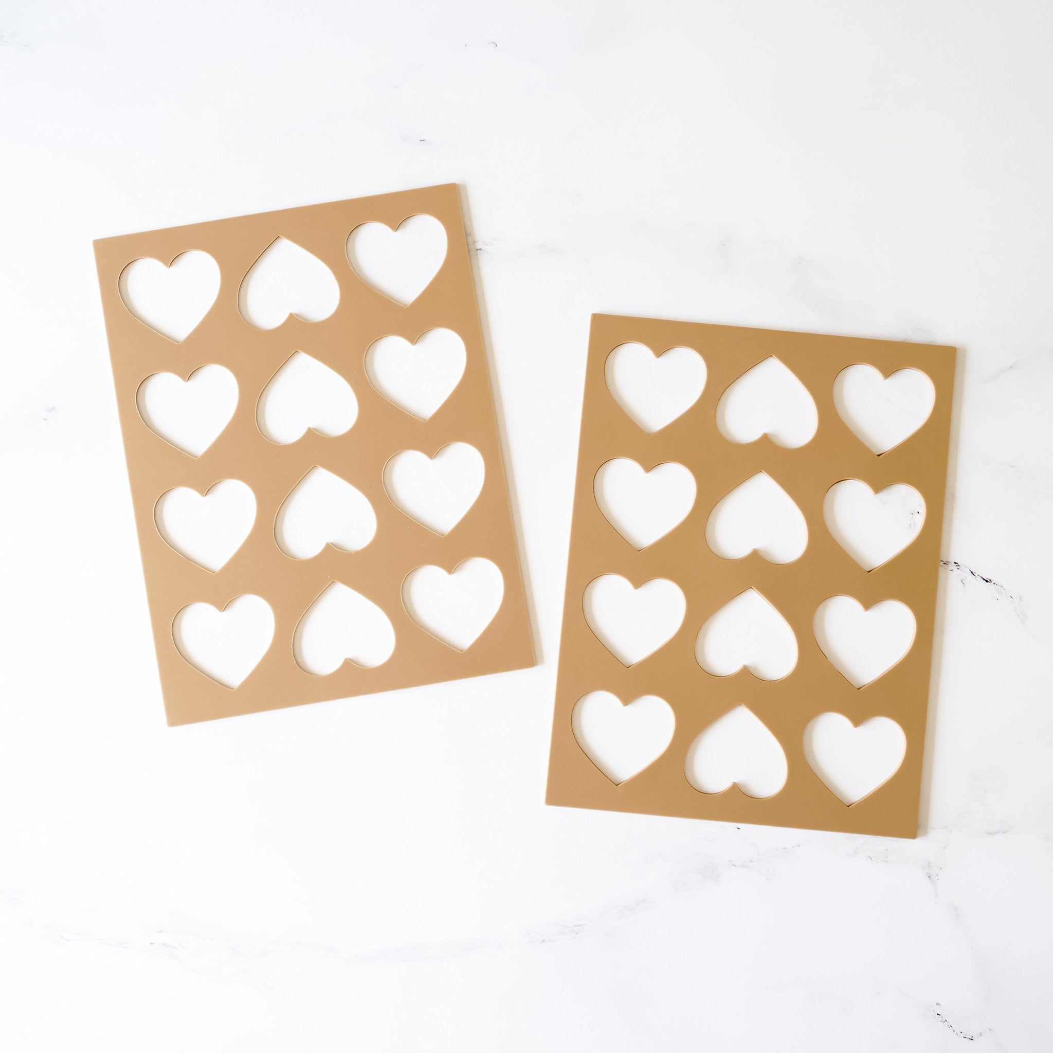 Two silicone cookie stencils with shapes for hearts, laid out on a white surface.