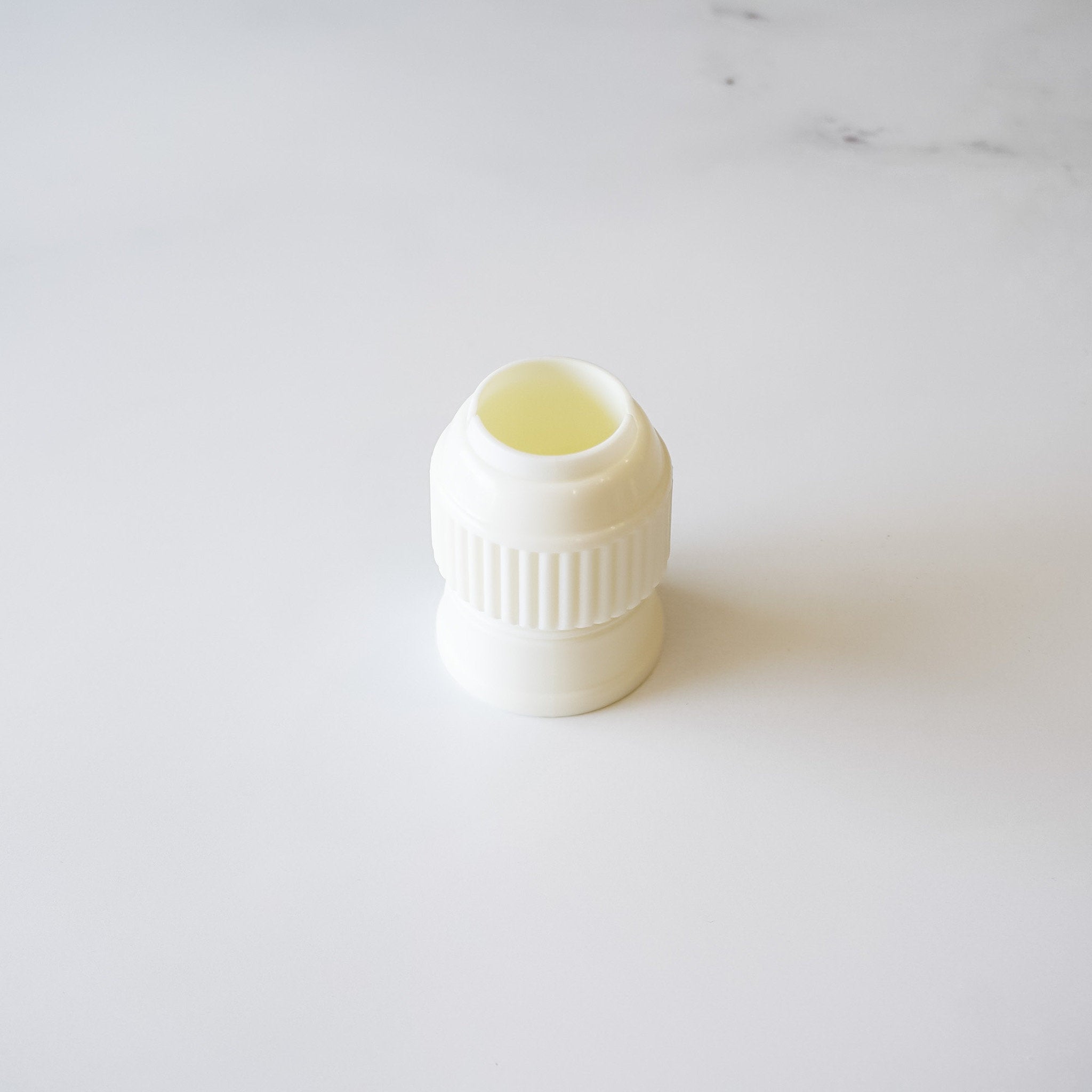 A white, 2-piece large plastic coupler for interchangeable piping tips in baking.