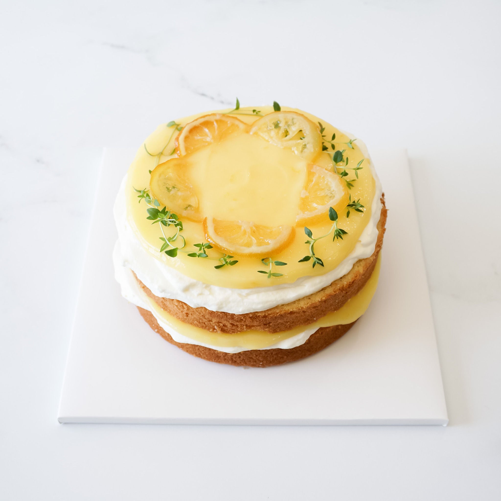 A lemon curd cake presented on a white square cake board with a matte finish.