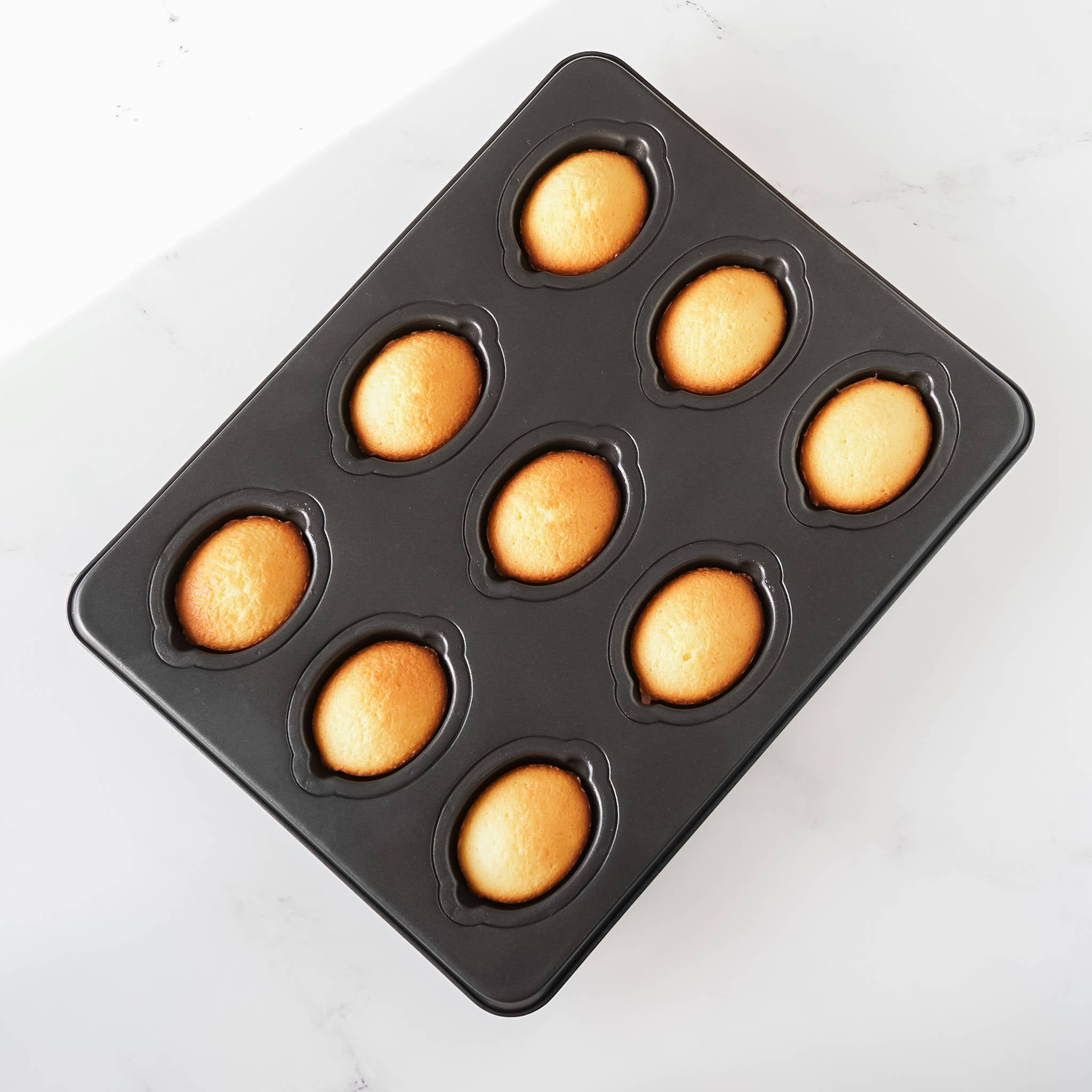 A black Lemon Cake Pan with nine cavities, each containing a small lemon-shaped cake.