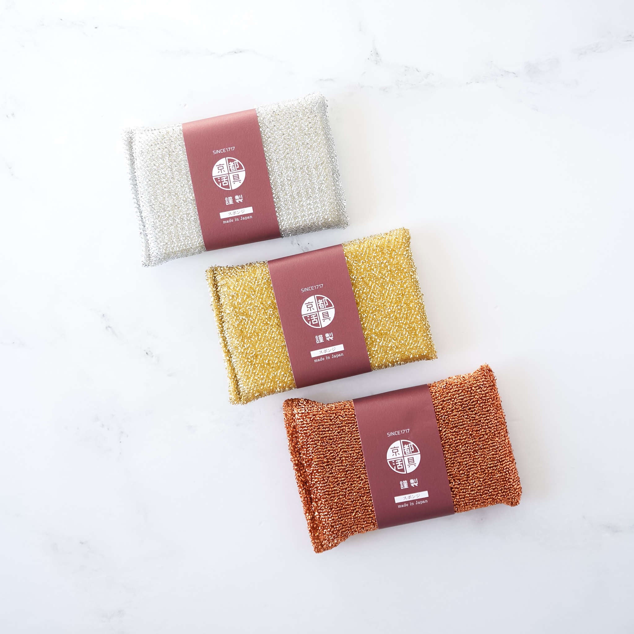 Three metal scrub sponges in gold, silver, and copper colors, packaged with labels.