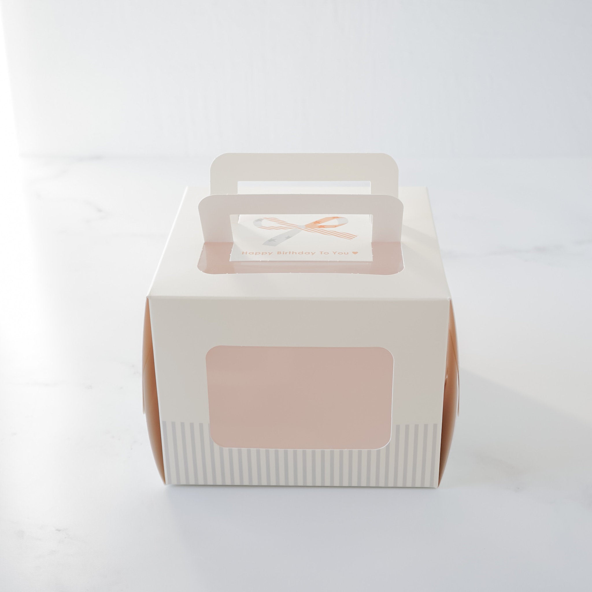 A closed Mini HBD Cake Box with a clear window displaying a &