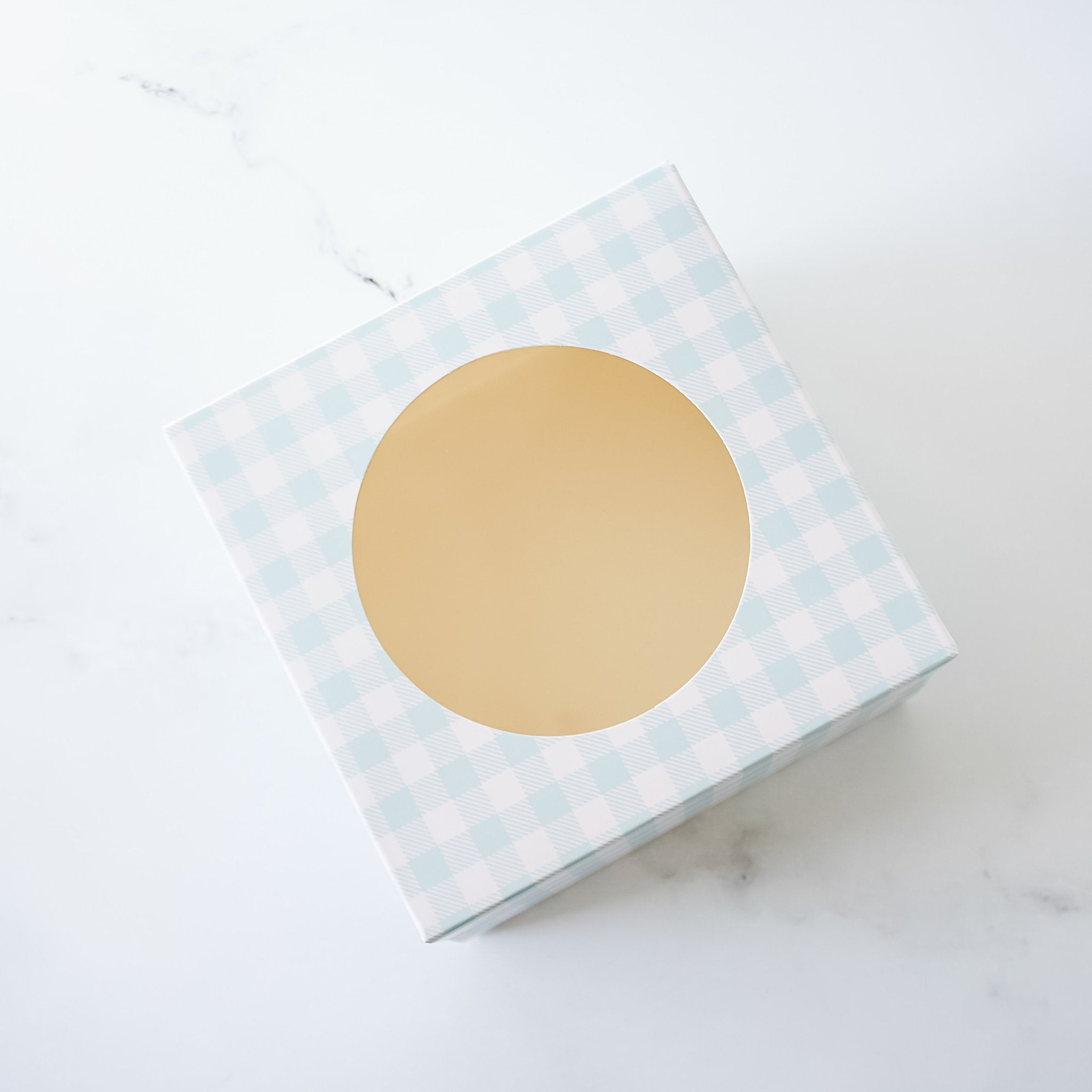 A white gift box with a light blue and white checkered pattern. The box has a circular cutout in the center.