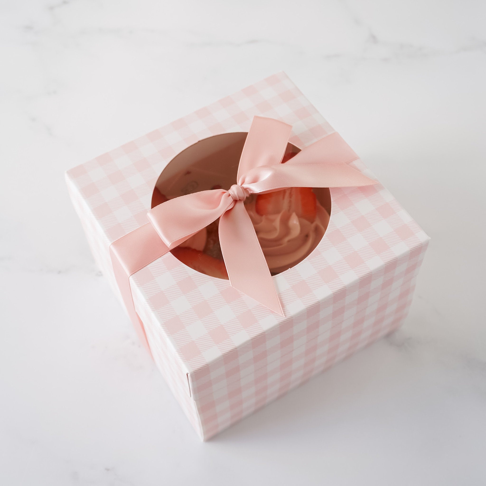 A pink and white gingham gift box with a window and a pink satin ribbon bow.