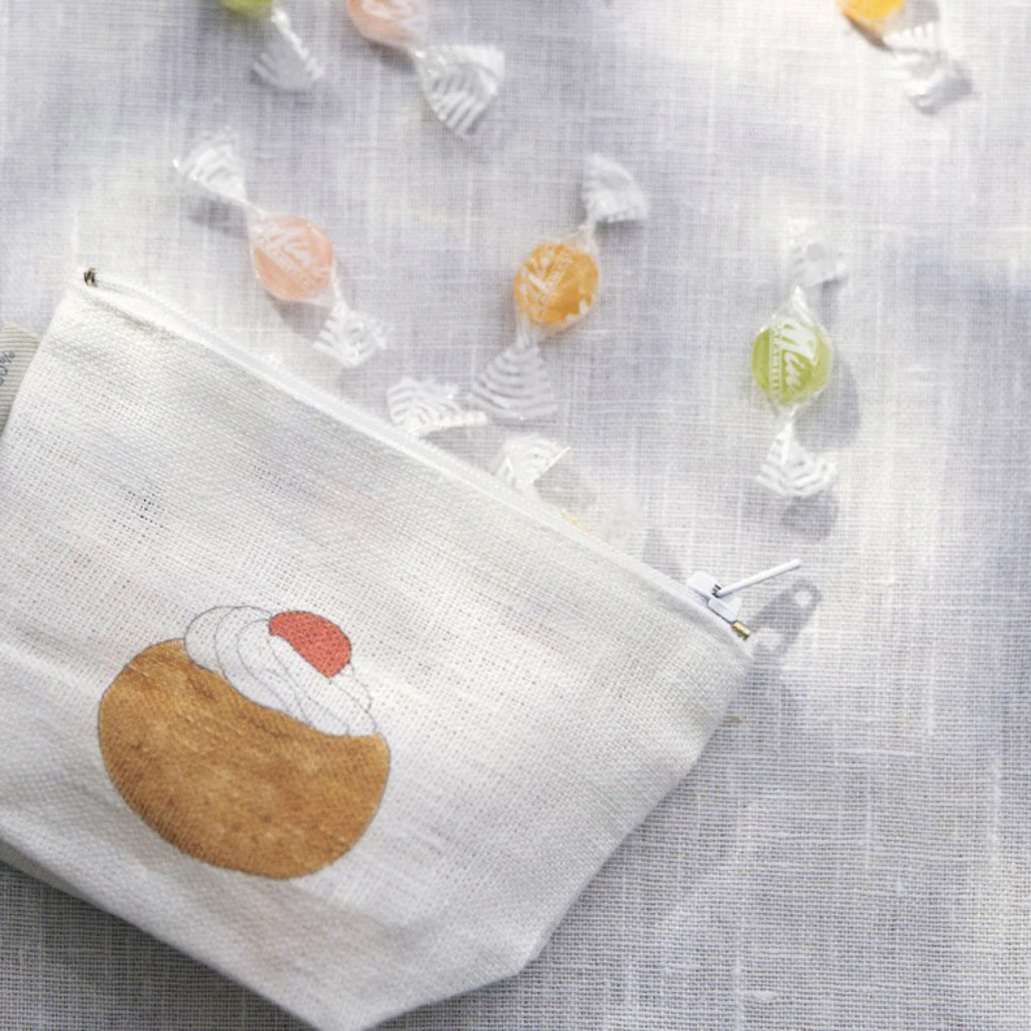 White pouch with a dessert design on a textured surface with candies around